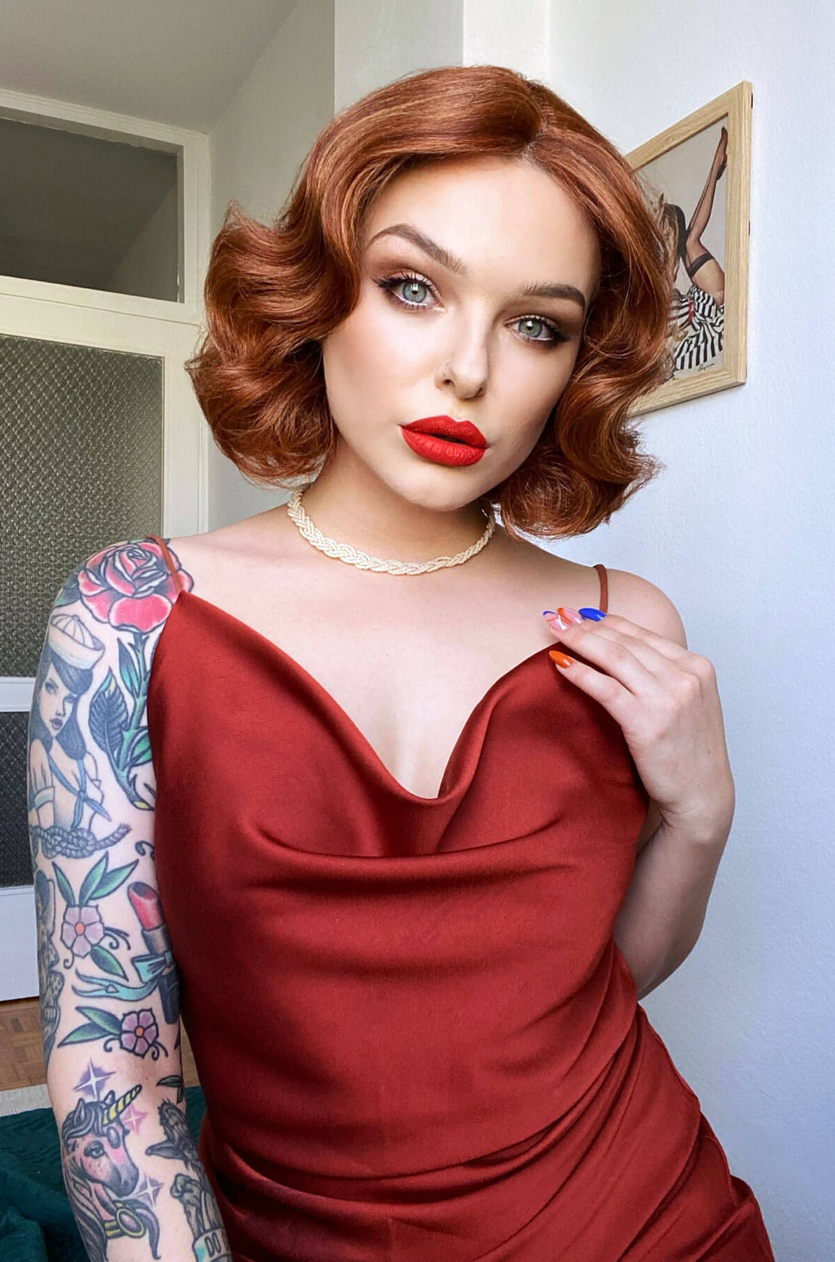 Woman in a red dress with tattoos on her arm, wearing a necklace. Red, auburn & blonde pinup wig, lace front, vintage style: Ginny