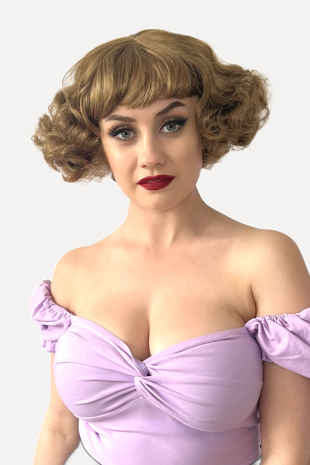 Woman with vintage-style hair and makeup wearing a purple dress against a white background. A short brown vintage style wig with waves: Rita golden brown 12-27