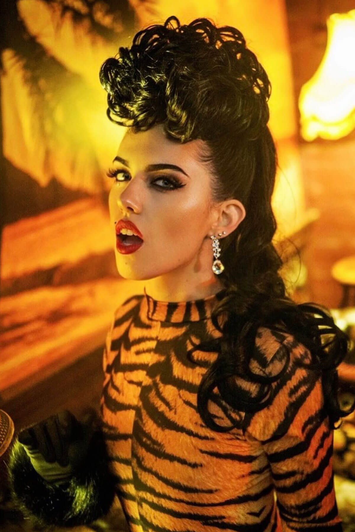 Woman with dark hair styled in an updo, wearing a tiger-striped outfit in a warm-toned setting. Hair poodle clip-in hairpiece bun vintage style 1950s: Lucille black 1B