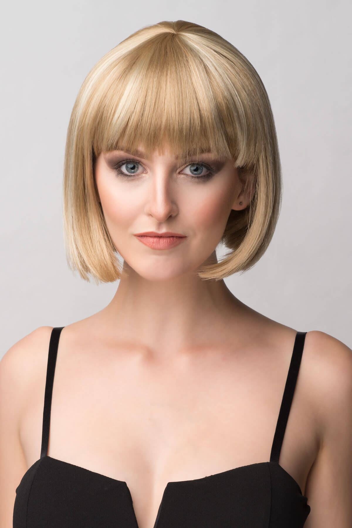 Woman with a blonde bob haircut against a plain background. Blunt blonde bob wig with fringe: Gracie