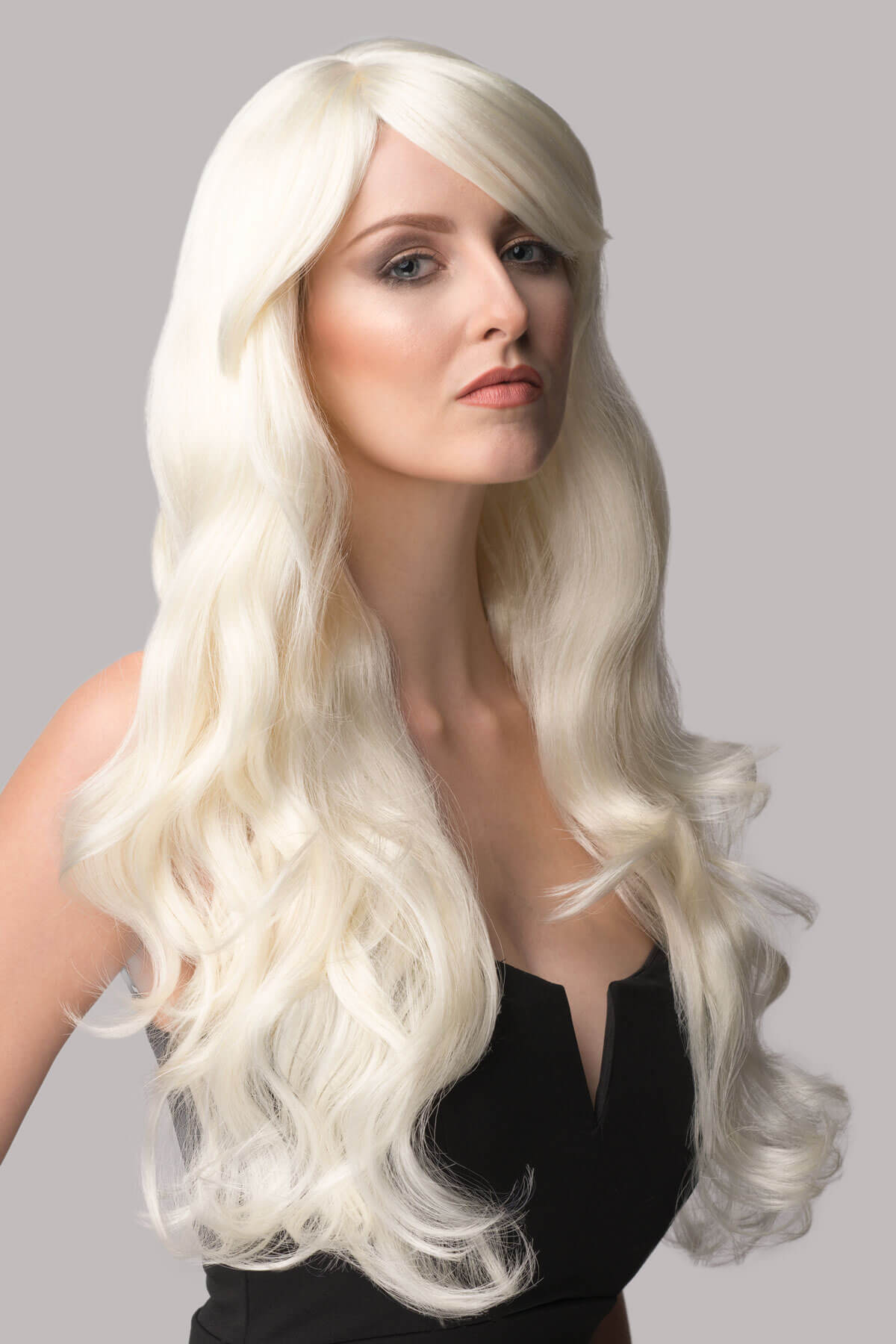Woman wearing a long blonde wig against a gray background. Long Platinum Blonde Wig (White Wig) Loose Curls: Andreana