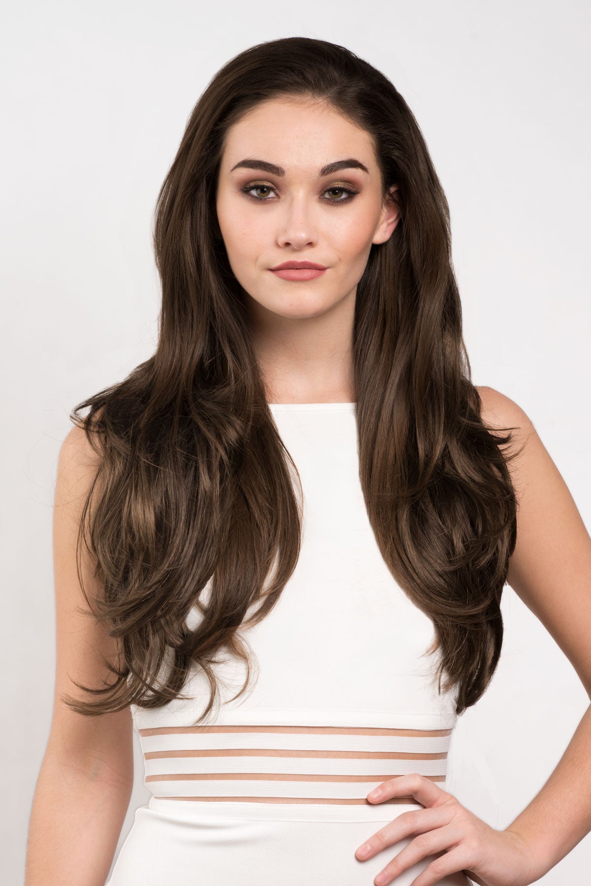 Woman with long brown hair wearing a white dress with gold stripes on a light gray background. Two-tone brown half wig hair piece, loose curls: Laila