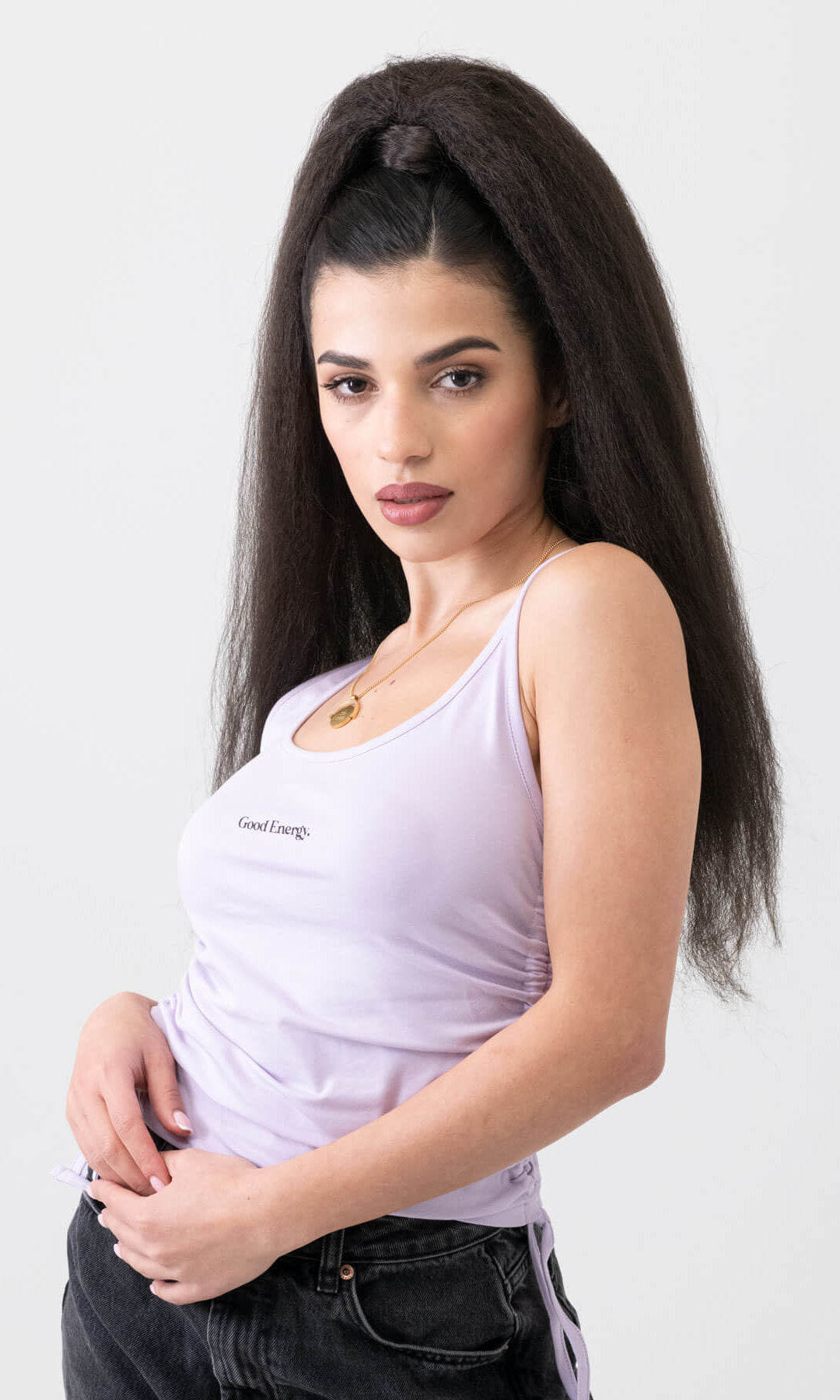 Woman wearing a white tank top with a logo on a plain background. Long Yaki perm ponytail extension with tight kinks and waves: Indi dark brown 4