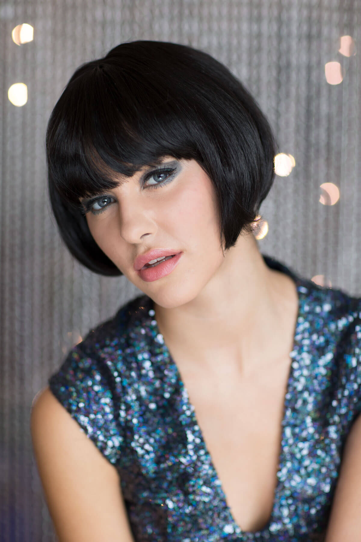 Woman with a stylish haircut and makeup wearing a sequined dress against a decorative background. Louise Brooks style wig, short black bob: Brooks