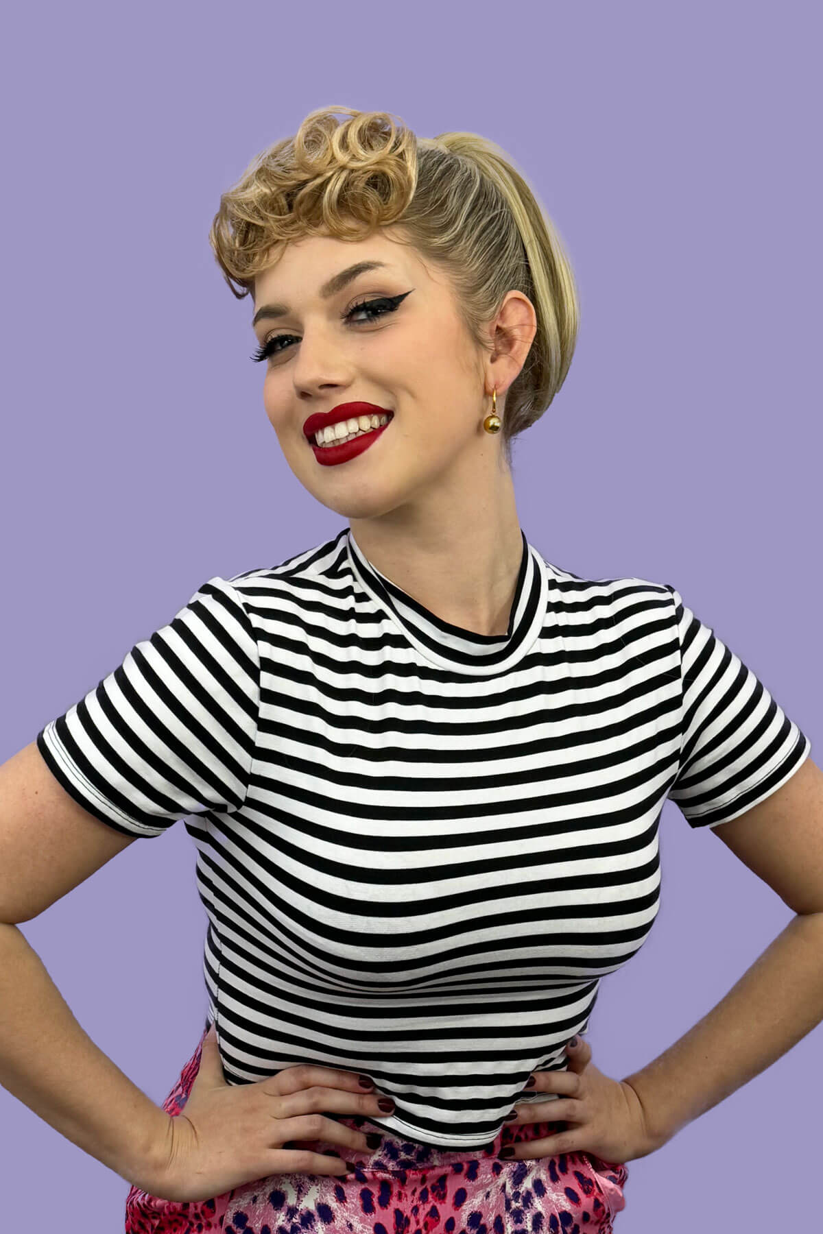 Woman wearing a black and white striped shirt with a purple background. Curly 1940s style clip-in fringe hairpiece/clip-in bangs: Bunny blonde 613T24