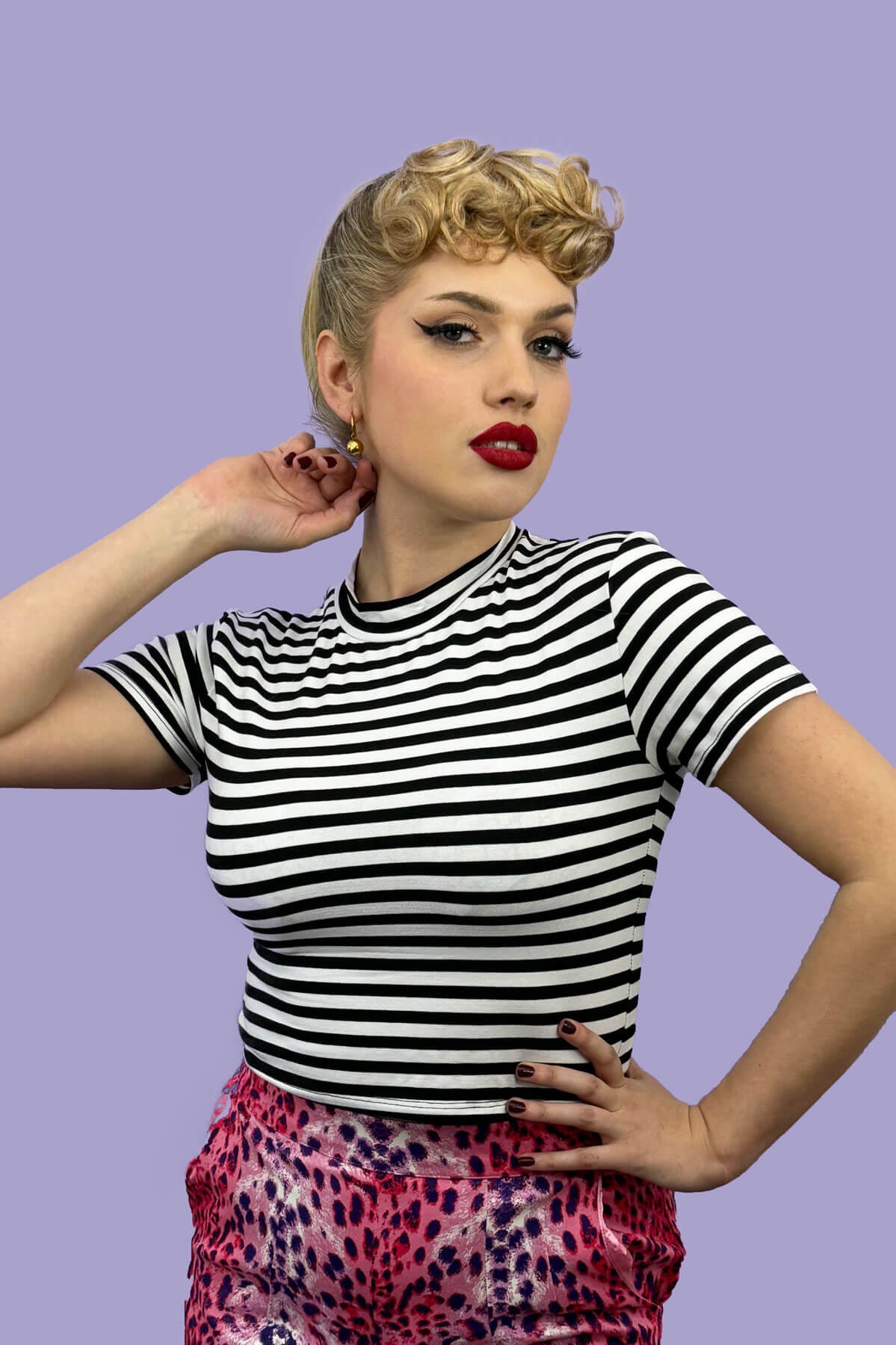 Woman wearing a black and white striped shirt with colorful pants against a purple background. Curly 1940s style clip-in fringe hairpiece/clip-in bangs: Bunny blonde 613T24