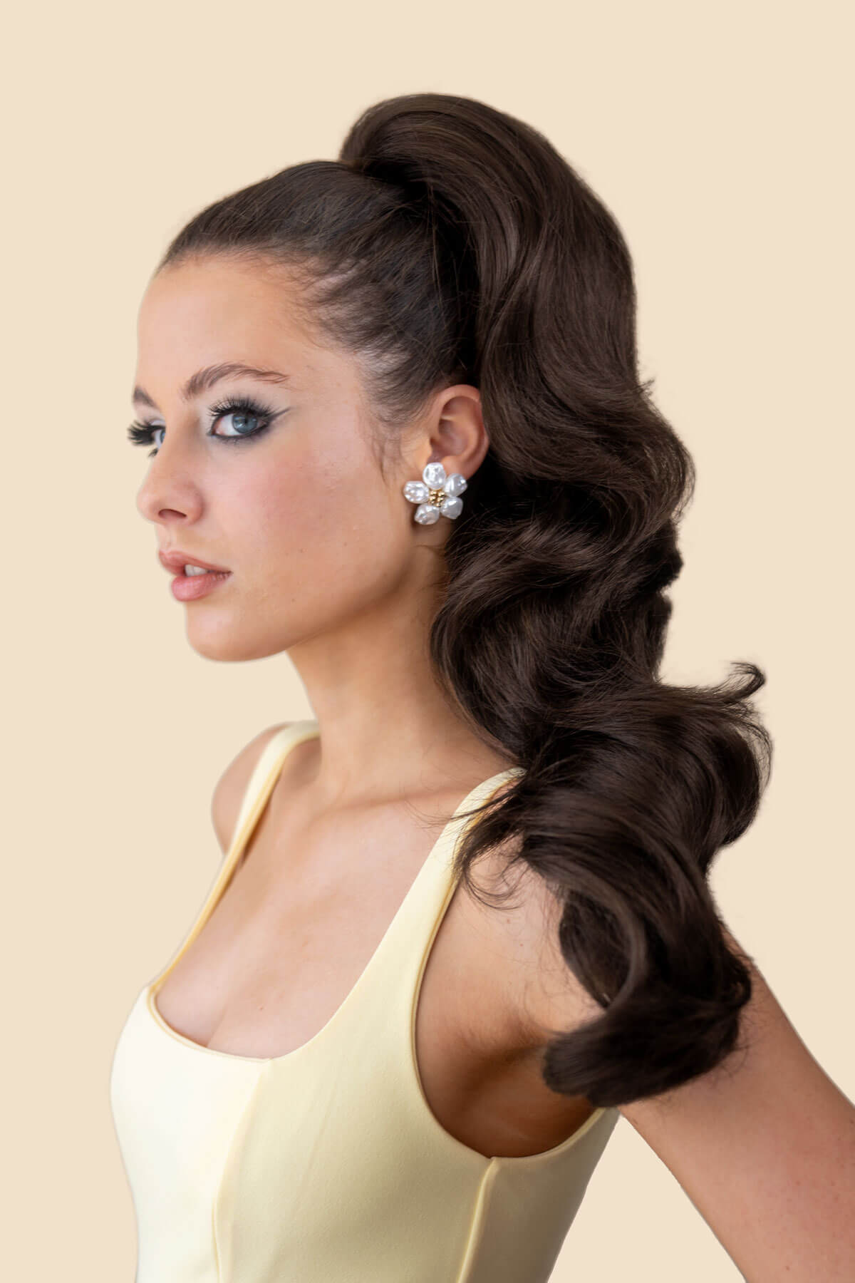 Woman with styled hair in a ponytail with a long, waved ponytail against a beige background. Double volume hairpiece extension with gentle waves: Naomi dark chocolate brown 6