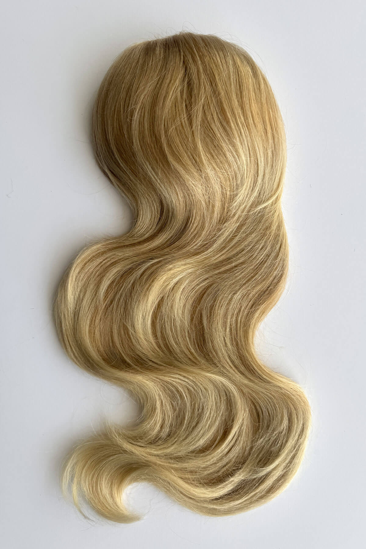 A wavy blonde hair piece with highlighted streaks, styled in loose curls, shown against a plain light grey background. Double volume hairpiece extension: Naomi blonde 613T24