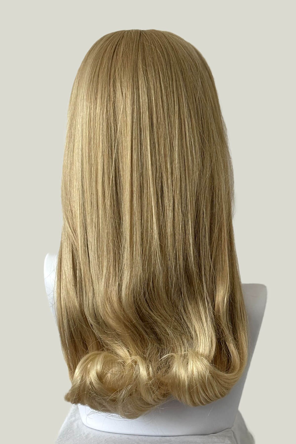 Blonde wig on a mannequin head against a plain background. 1960s Retro high crown, half wig hairpiece, long with hair flip: Priscilla blonde 613T24