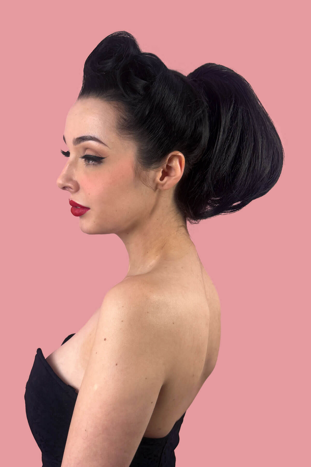 Woman with styled hair, with short ponytail against a pink background. Short beehive ponytail hairpiece: Sherri black 1B
