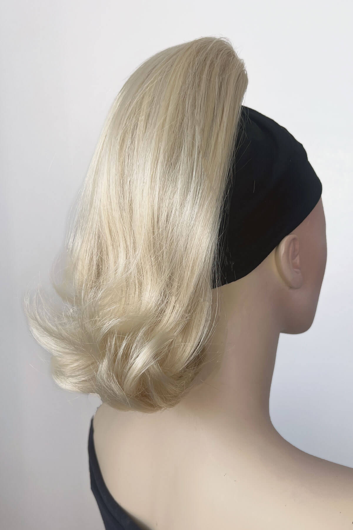 Blonde wig on a mannequin head with a black headband against a white background. Ponytail hairpiece, shoulder length with flick/flip, retro 1960s style: Ariana creamy blonde 613