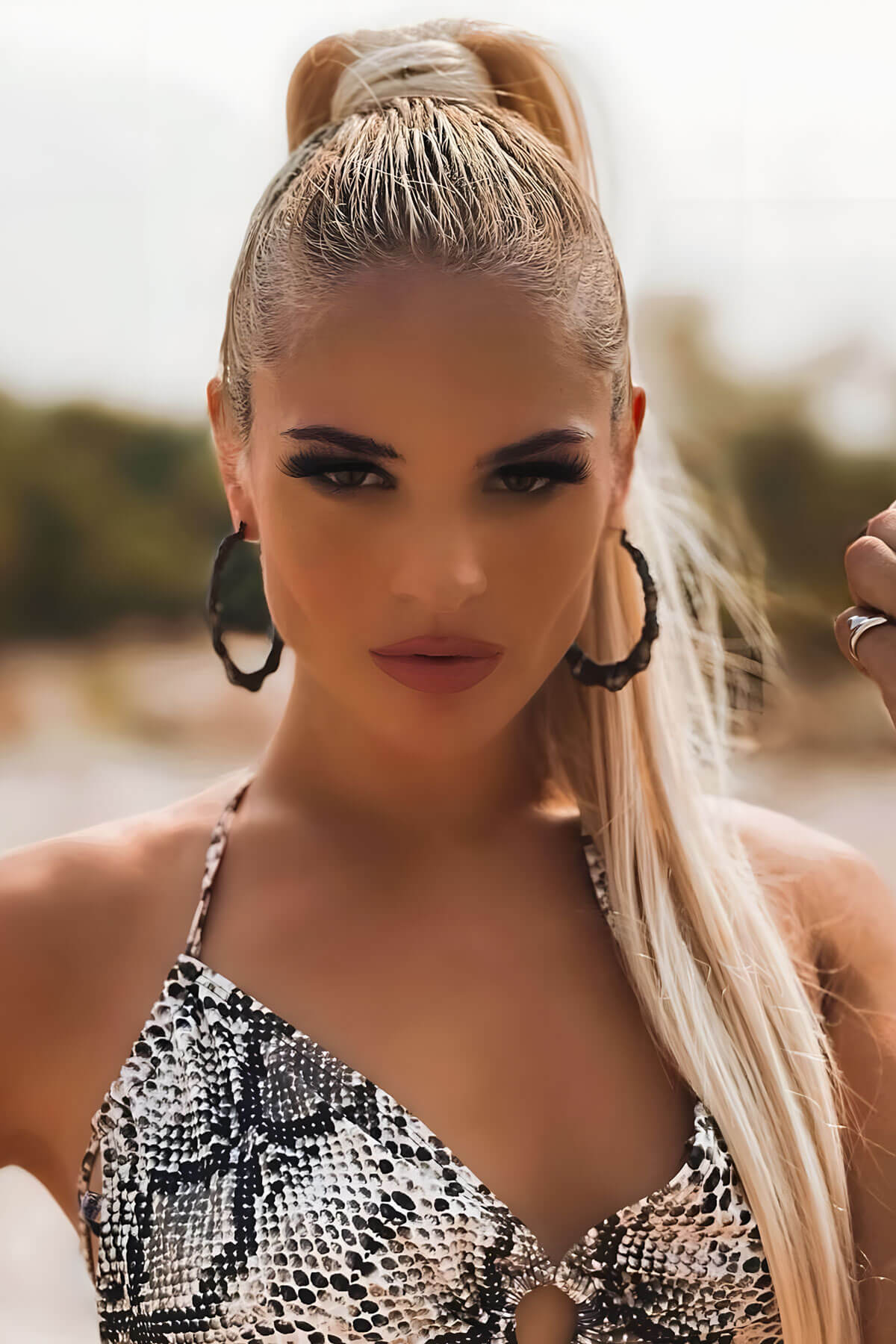 Woman with styled hair and snake print top outdoors. Long sleek ponytail extension with gentle, layered waves: Mali champagne blonde 613