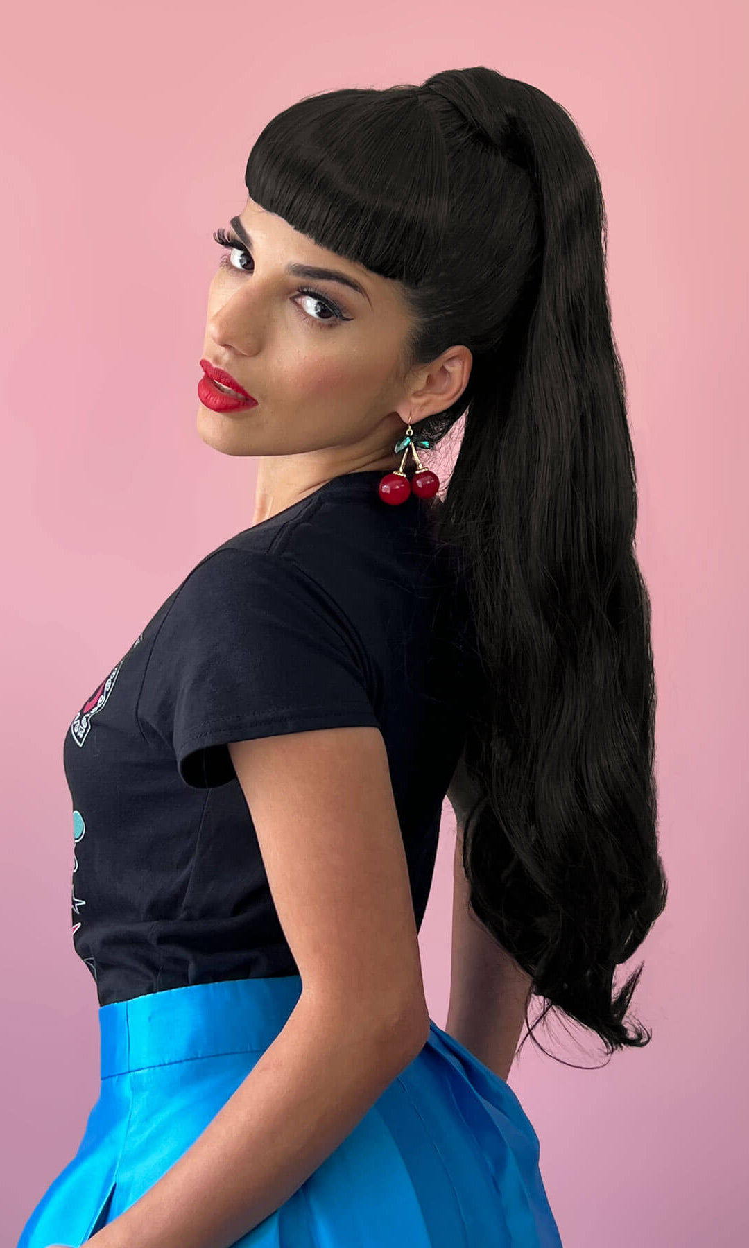 Woman with long black hair styled in a high ponytail, wearing a black top and blue skirt on a pink background. Long ponytail extension with soft waves: Sophie black 1b