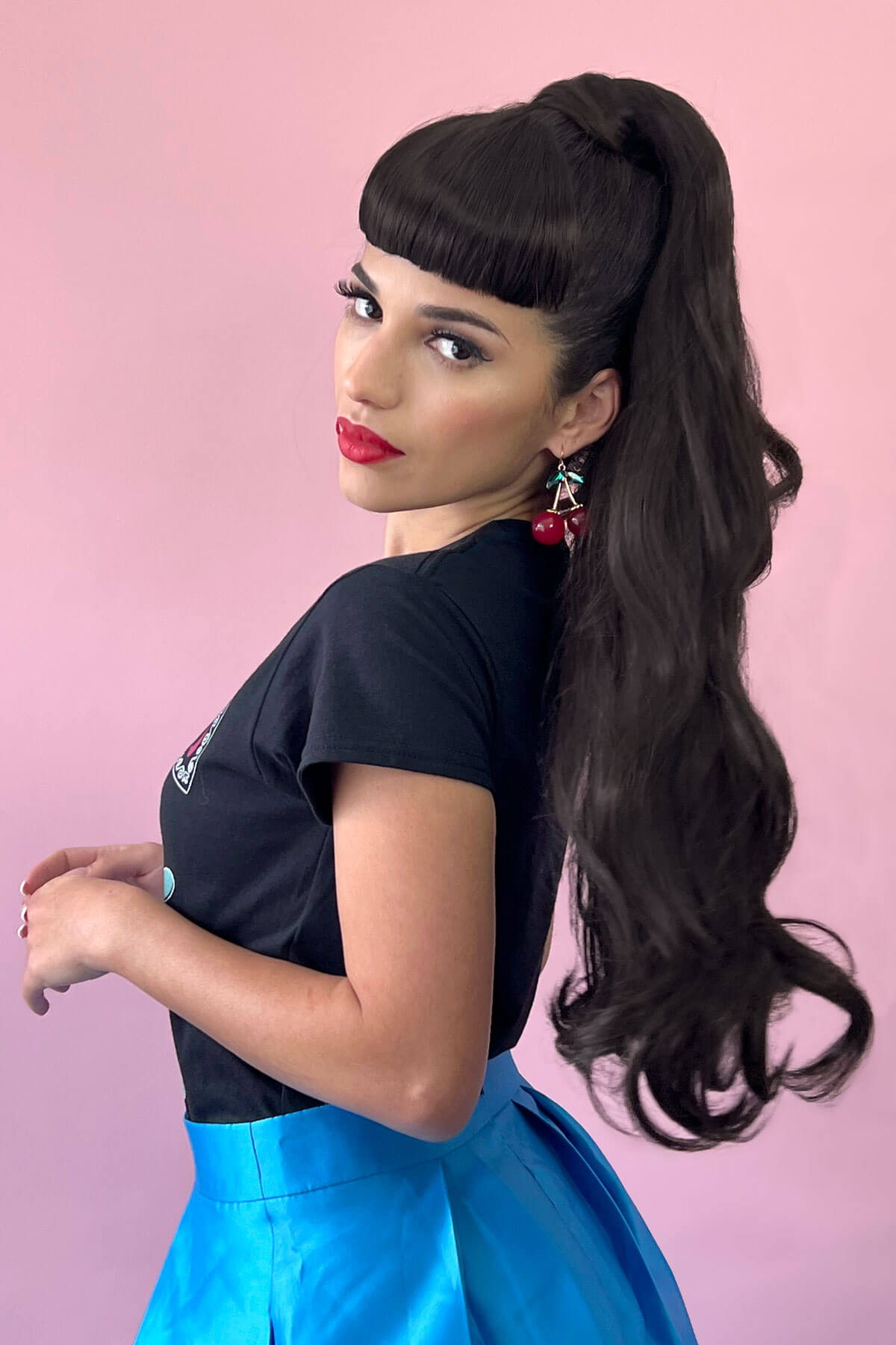 Woman with long dark hair styled in a high ponytail against a pink background. Long ponytail extension with soft waves: Sophie dark brown 4