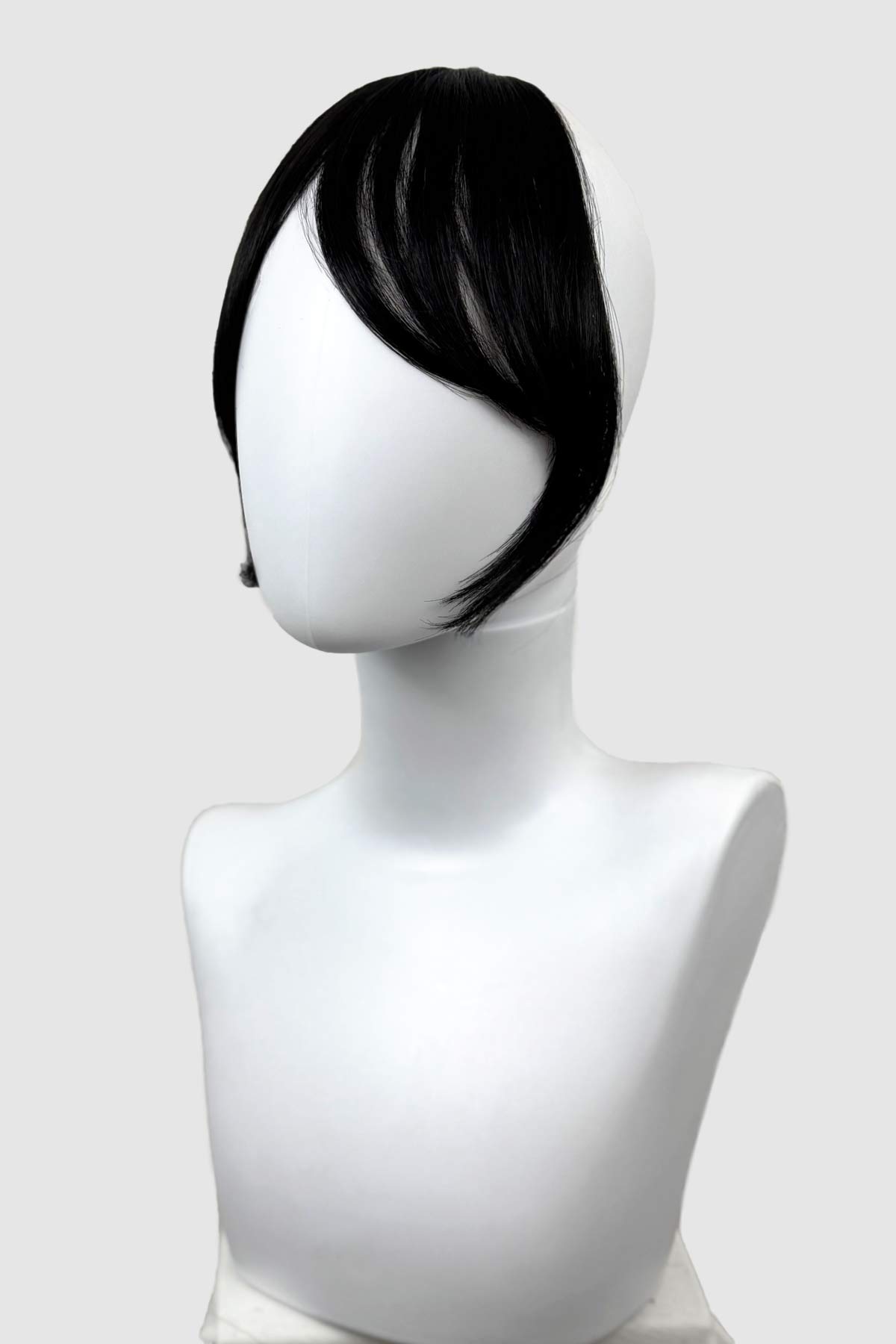 Black wig on a white mannequin head against a white background. Clip in fringe hairpiece/clip-in curtain bangs, with long, face framing wisps: Sabrina black 1b