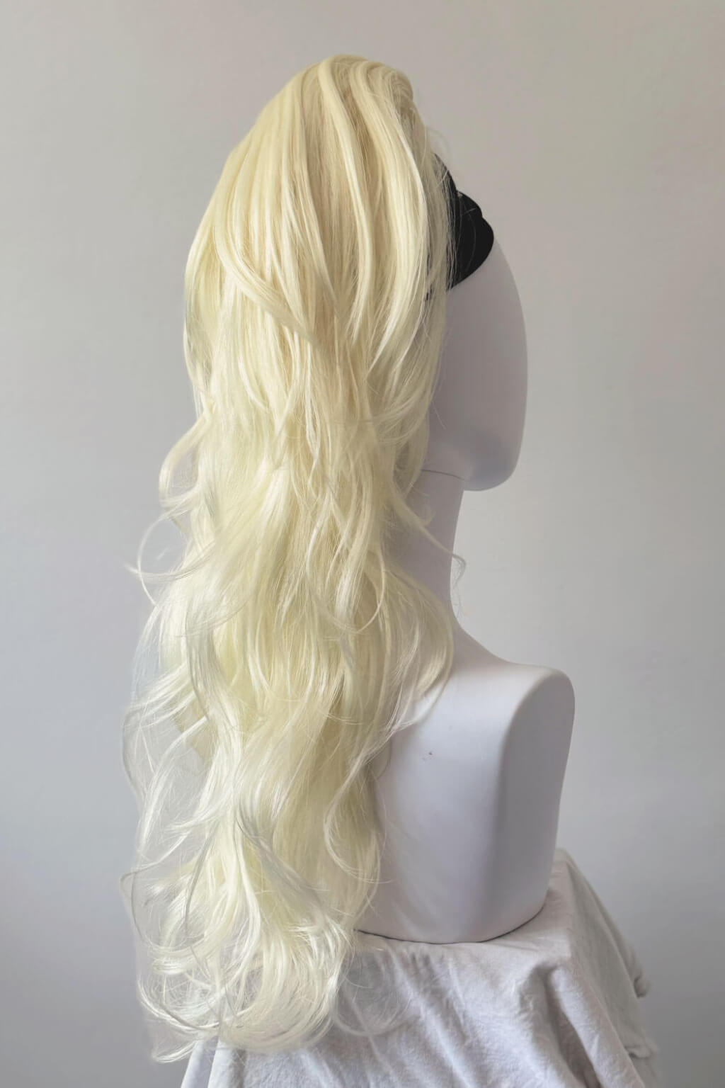 Blonde wig on a mannequin head against a white background. Clip-in ponytail hairpiece extension: Olivia platinum blonde 1001
