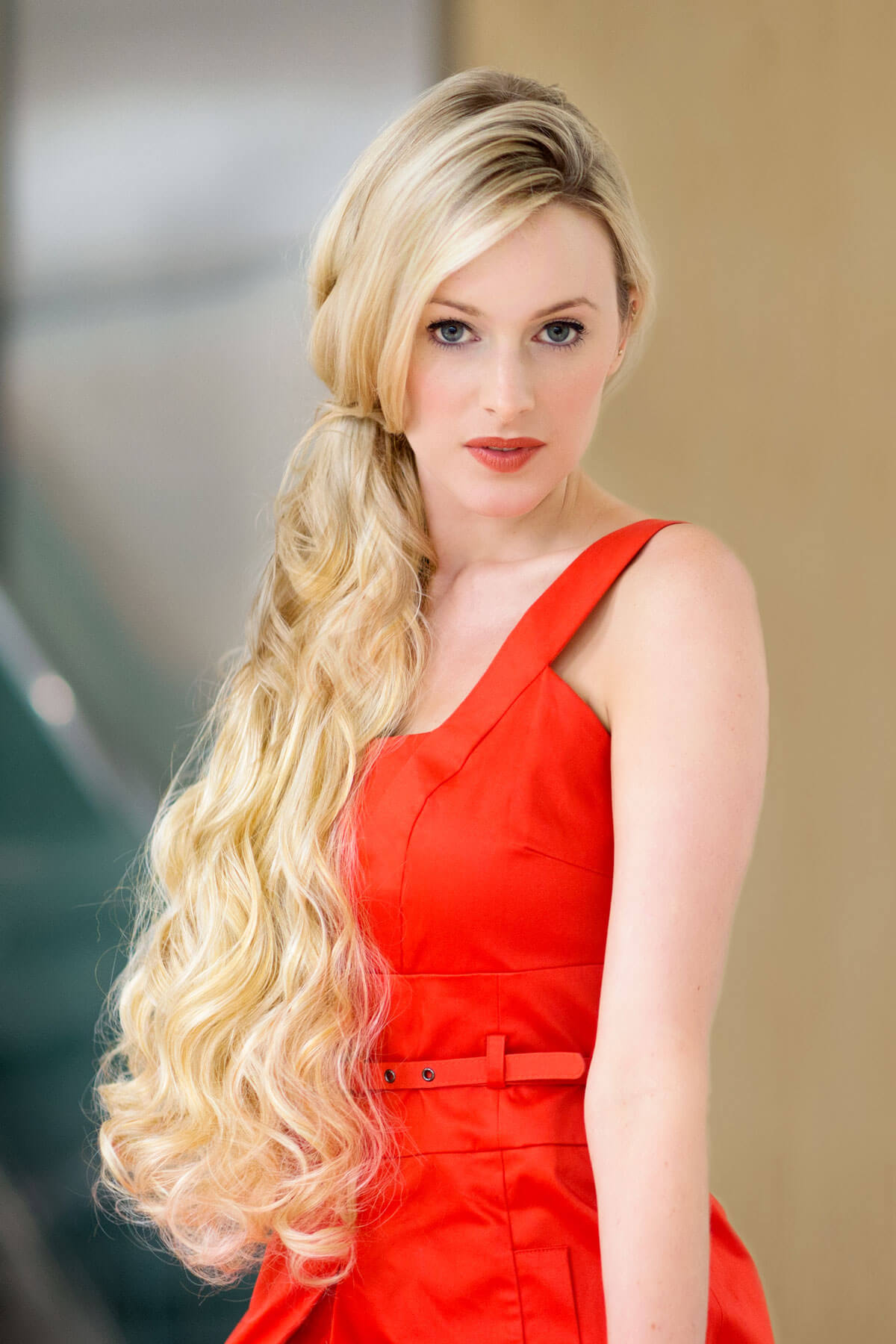 Woman in a red dress with long blonde hair against a blurred background. Extension hairpiece, long, versatile, Flexihair: Cristina honey blonde 24BH613