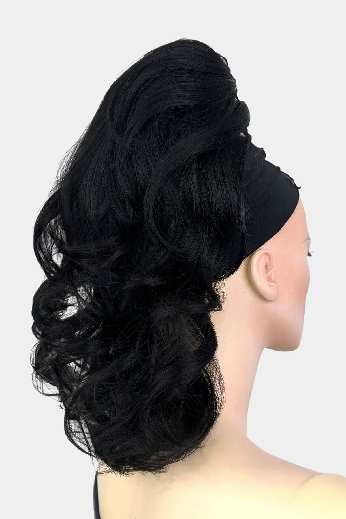 A mannequin wearing a curly ponytail extension hairpiece with loose, layered curls. It is seen from the shoulders up, with a backdrop featuring bokeh lights. Curly ponytail extension clip-on hairpiece: Tulisa black 1B