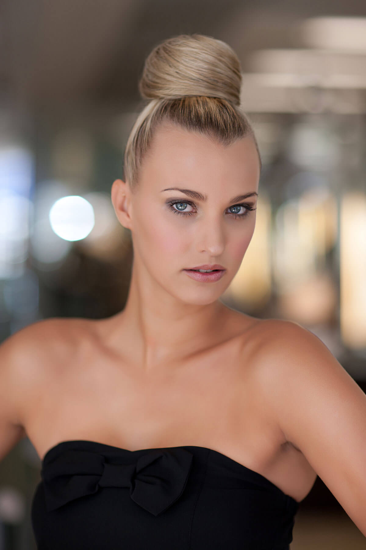 Woman with styled hair wearing a black strapless dress against a blurred background. Hair bun hairpiece; instant perfect hairbun: Hebe