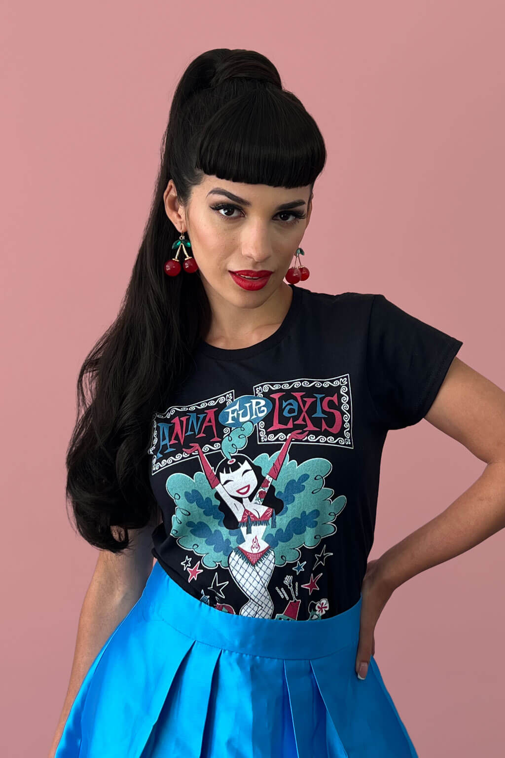 Woman wearing a black t-shirt with a colorful graphic design on a pink background. Clip-in fringe hairpiece/clip-in bangs, thick, straight retro rockabilly style: Ida chestnut black 1B