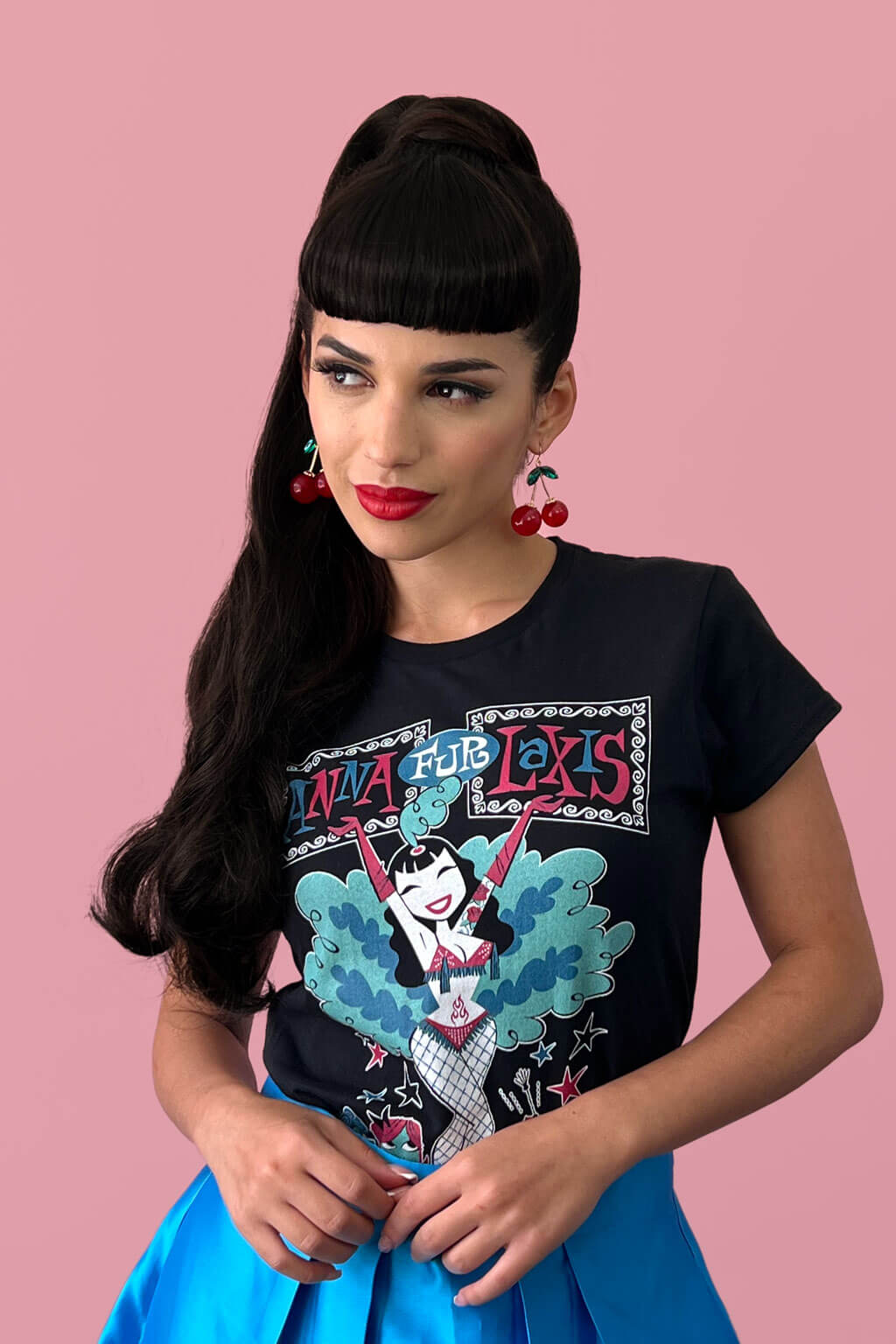 Woman wearing a black t-shirt with colorful graphic design on a pink background. Clip-in fringe hairpiece/clip-in bangs, thick, straight retro rockabilly style: Ida chestnut black 1B