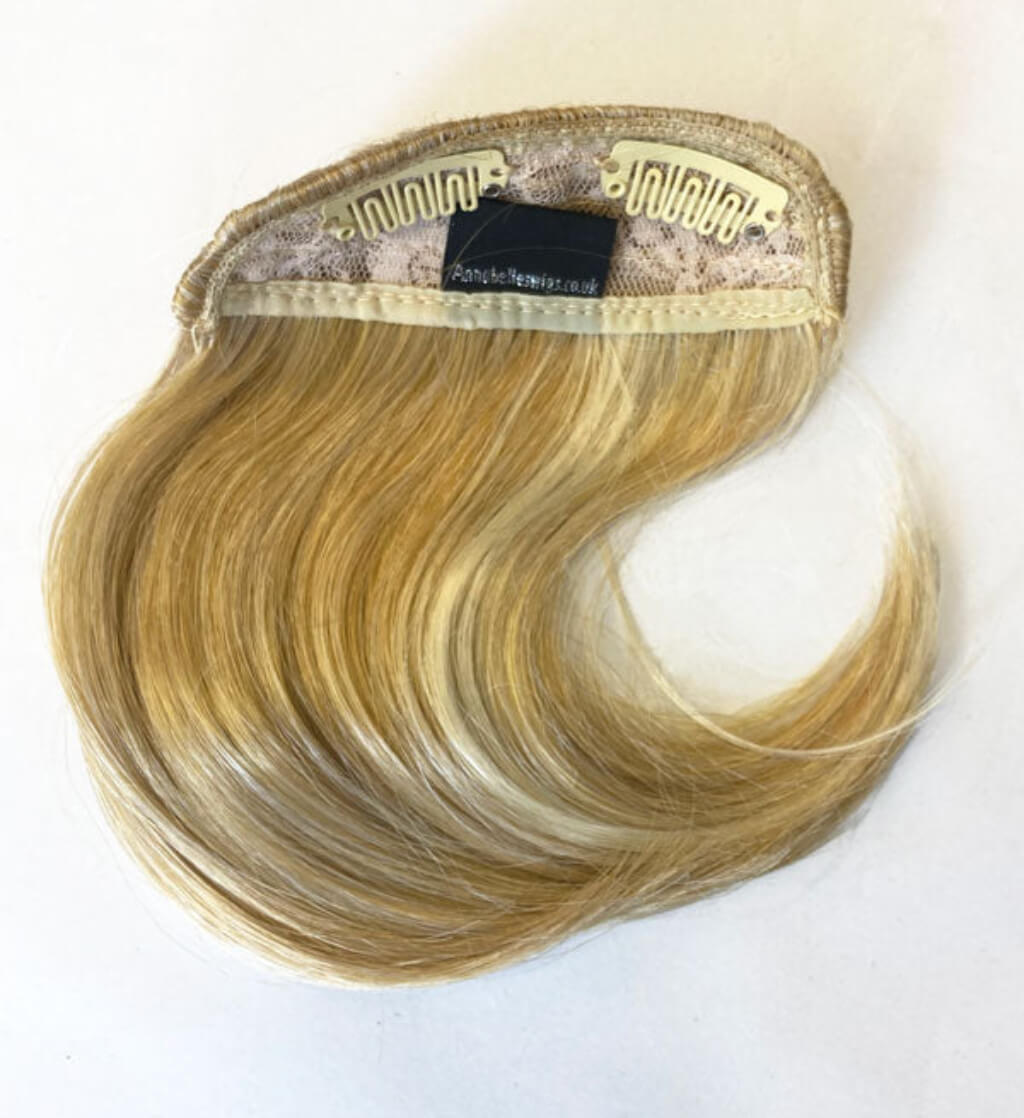 Blonde hair extension with a brand label on a white background. Clip-in fringe hairpiece, curved, side-sweeping: Eliana blonde 24BH613
