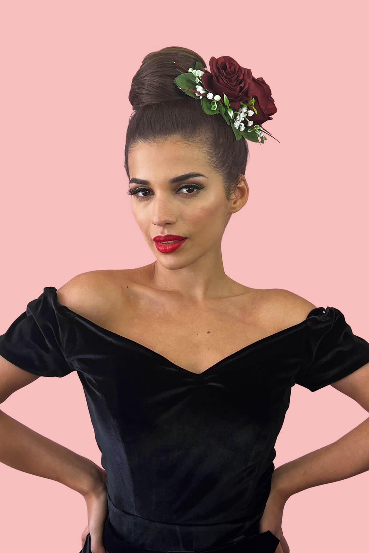 Woman in a black off-shoulder dress with floral headpiece against a pink background. chestnut brown hair bun