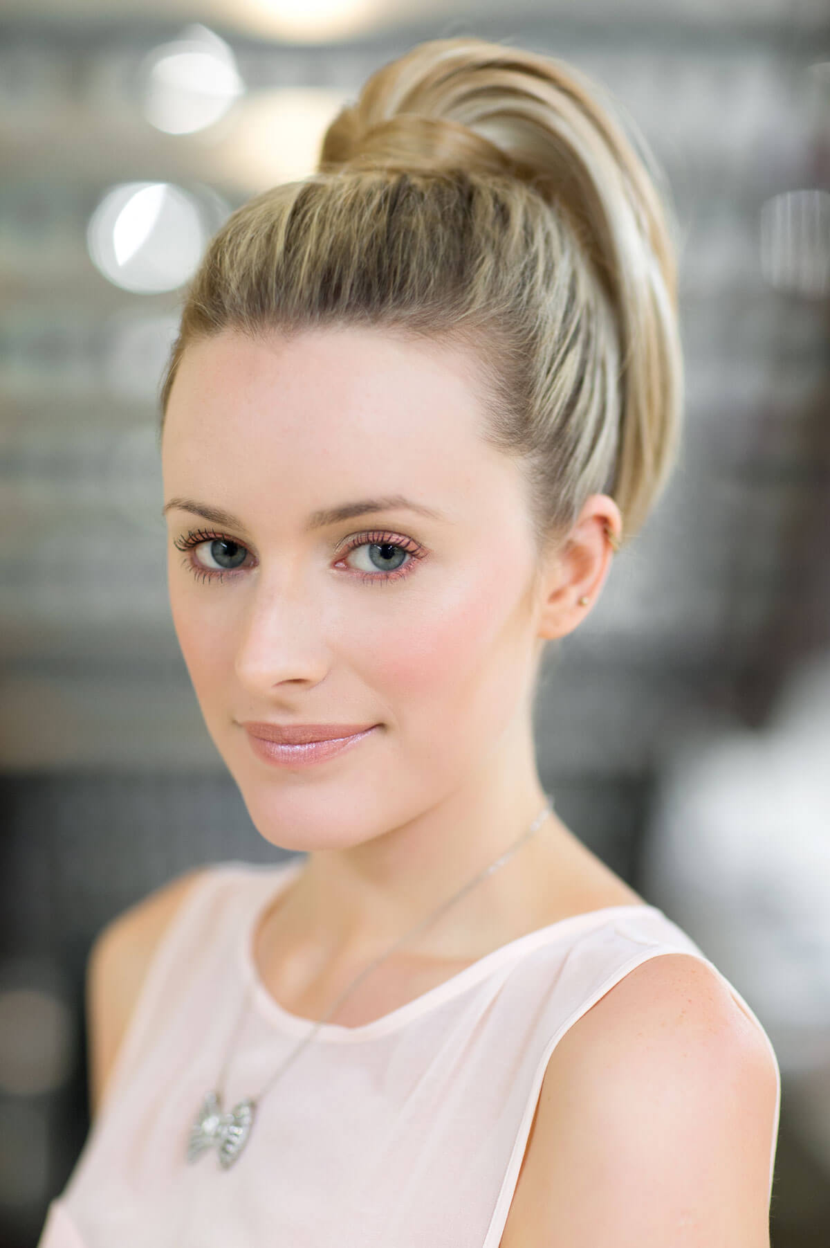 Woman with a high ponytail wearing a light pink dress against a blurred background. Sleek ponytail extension hairpiece, Flexihair: Jasmin