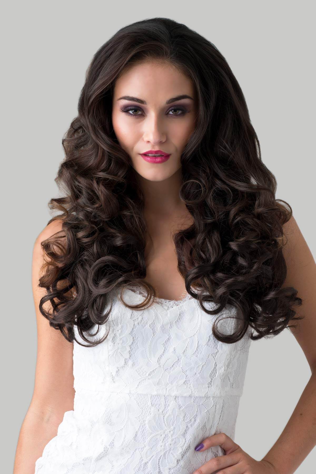Woman with long, wavy hair wearing a white dress against a gray background. Curly brown half wig hairpiece: Susan