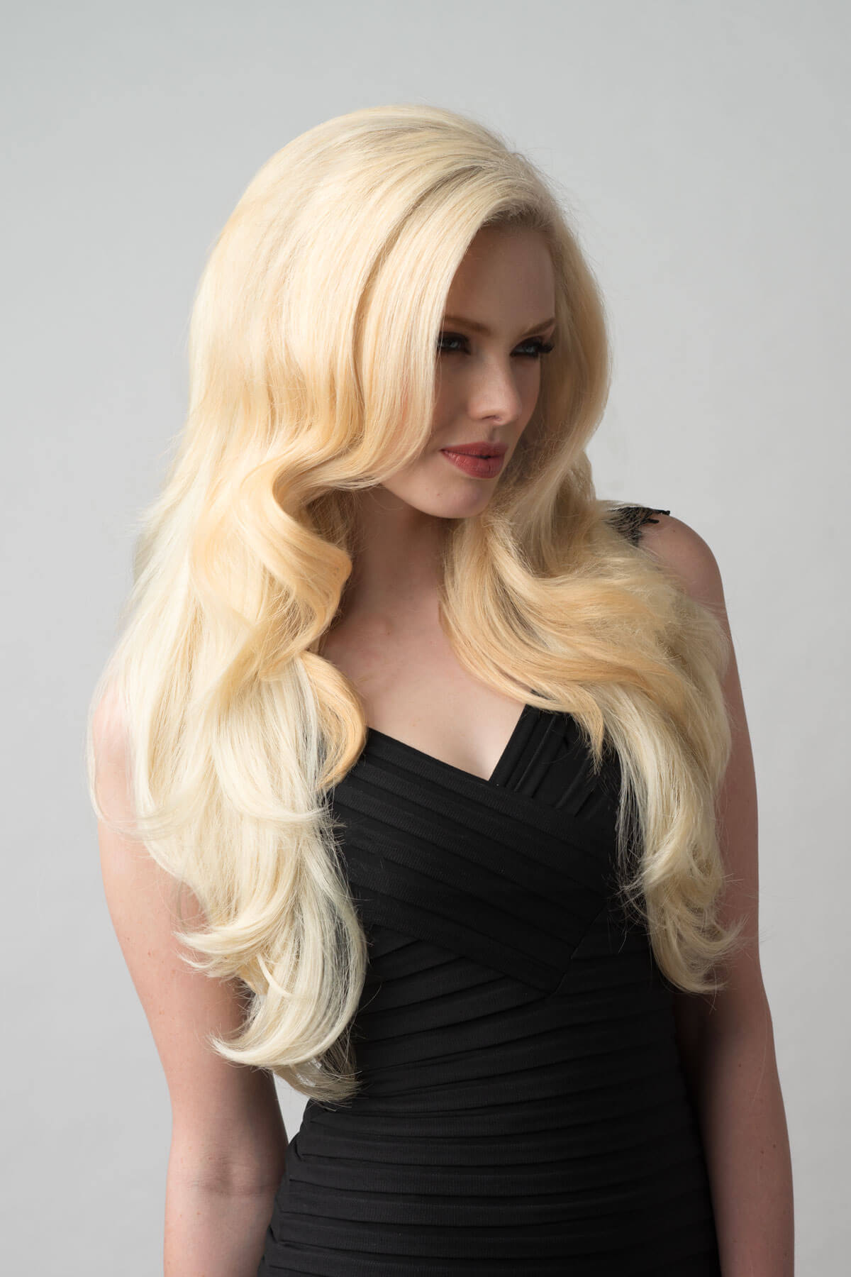 Woman with long blonde wig wearing a black dress on a gray background. Long blonde half wig hairpiece (3/4 wig) loose curls: Frankii creamy blonde 613