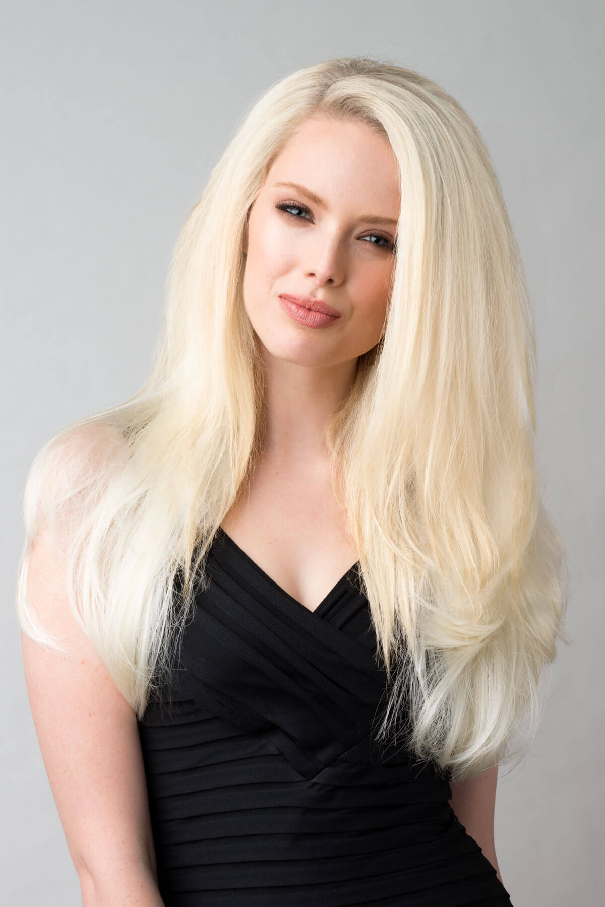 Woman with long blonde hair wearing a black dress against a gray background. Platinum blonde half wig hairpiece (3/4 wig), straight: Gwen
