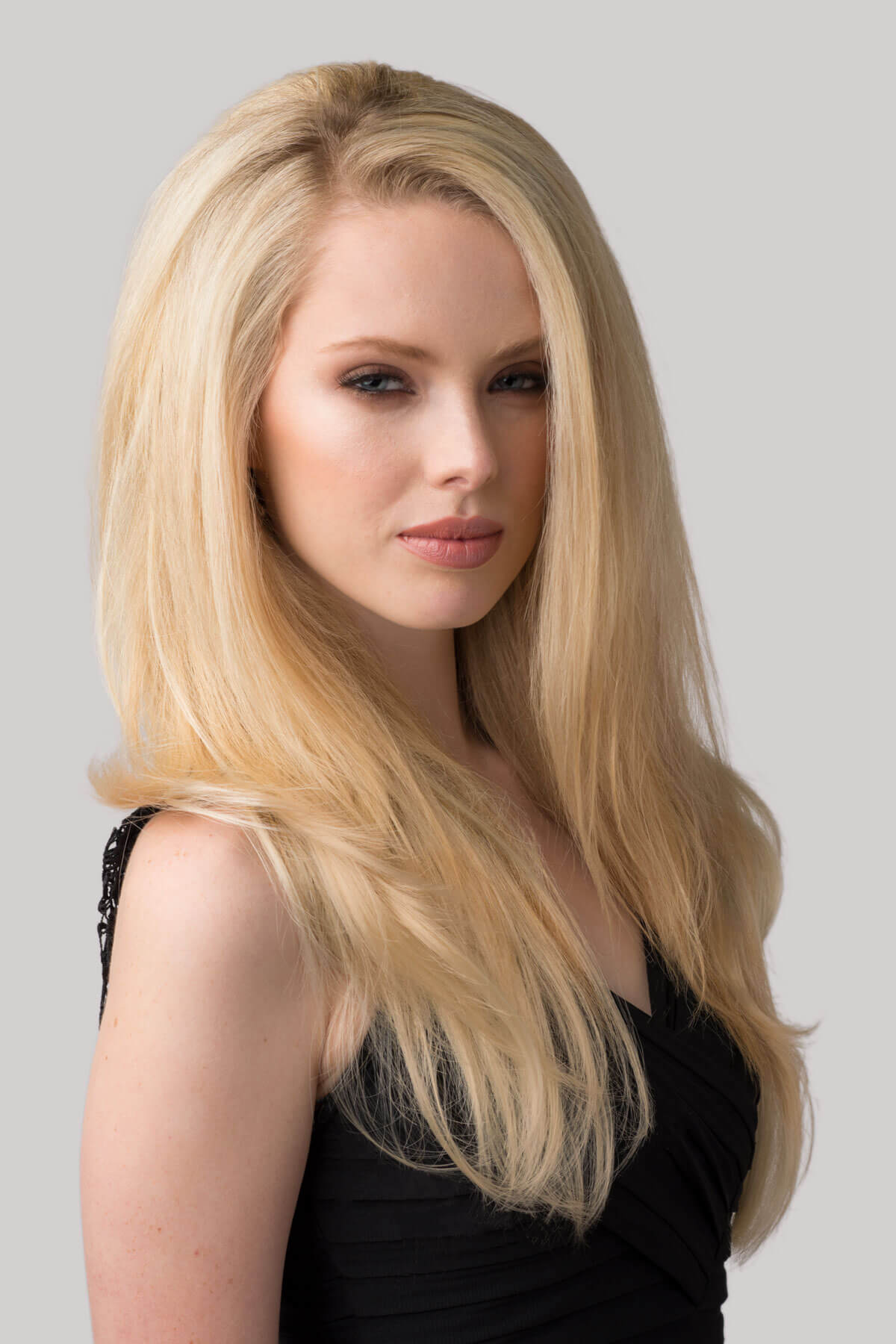 Woman with long blonde hair against a gray background. Straight blonde half wig hairpiece (3/4 wig), layered: Autumn blonde 24BT613