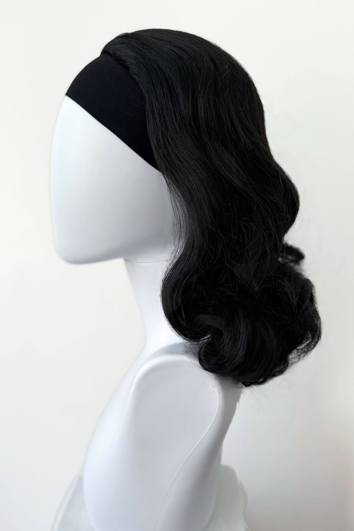 Black wig on a white mannequin head against a white background. 1950s style shoulder length half wig hairpiece with beautiful vintage waves: Onyx colour black 1B