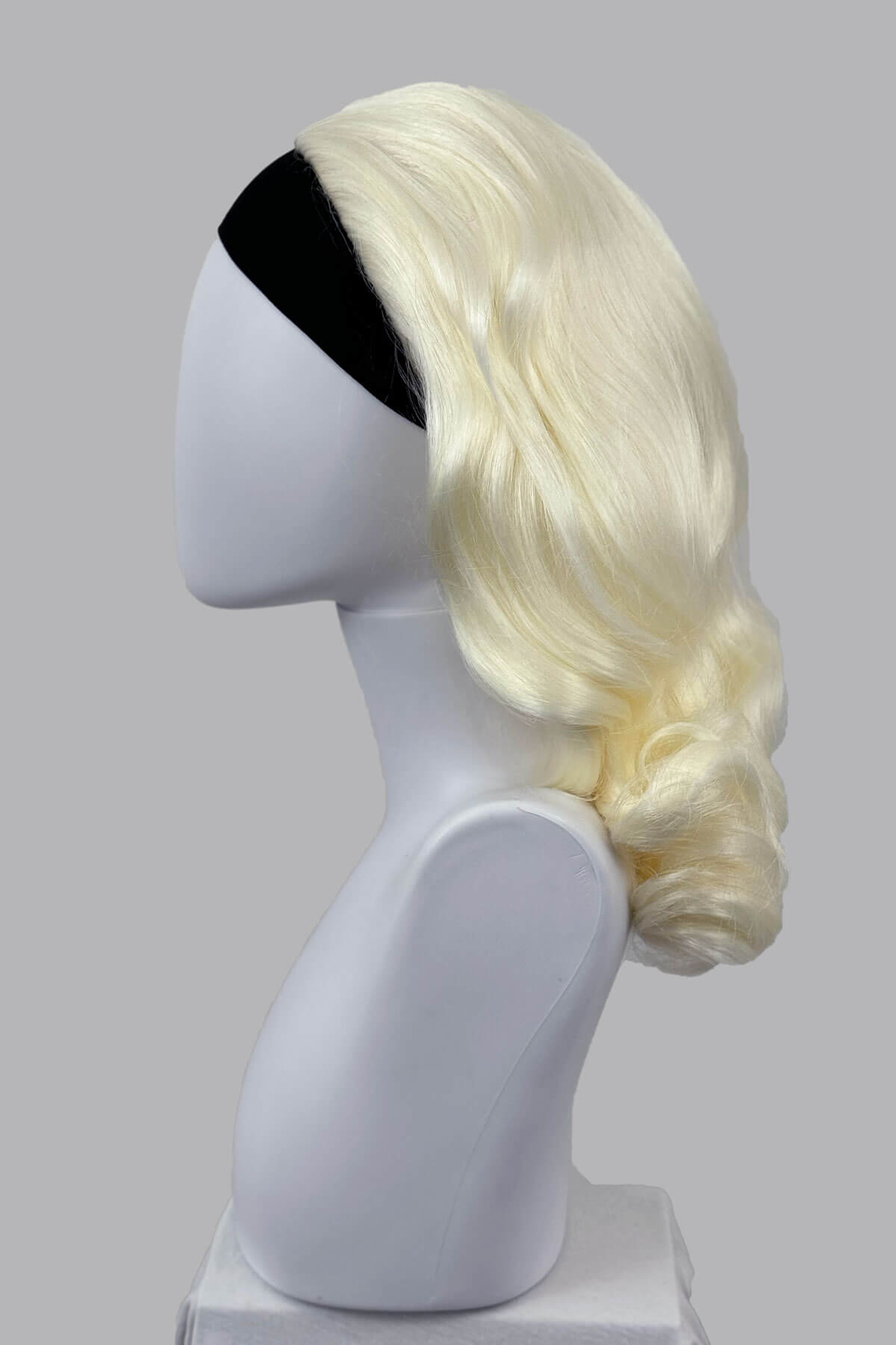 Blonde wig on a mannequin head against a grey background viewed from the side. 1950s style shoulder length half wig hairpiece with beautiful vintage waves: Onyx platinum blonde 1001