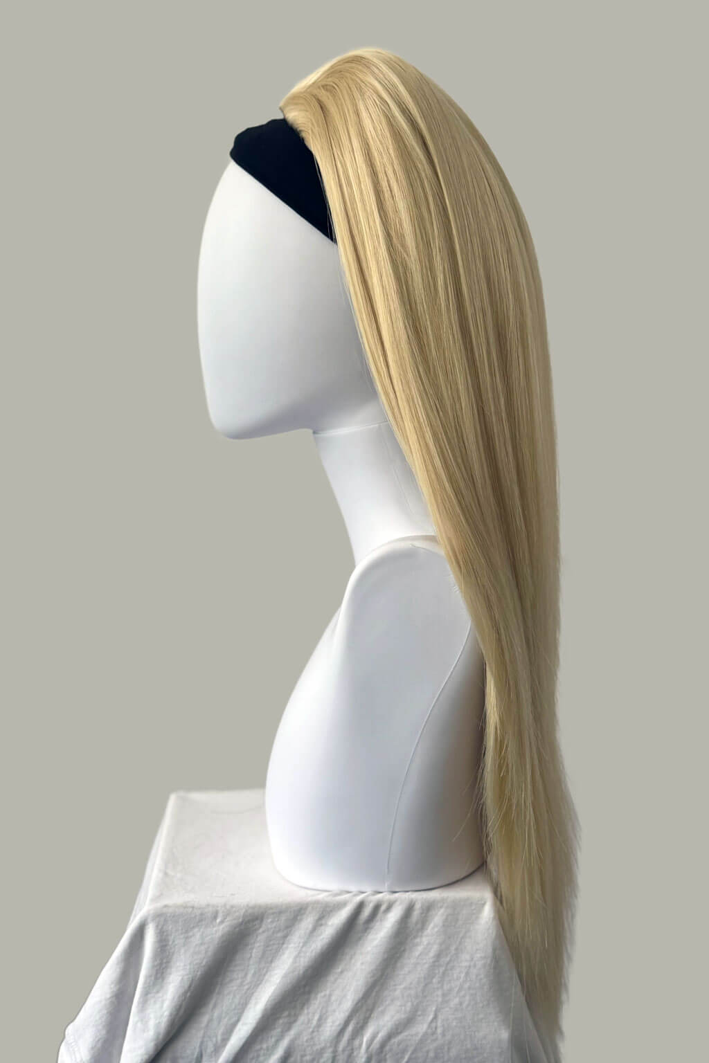 Blonde wig on a mannequin head against a plain background. 1960s style hair, high crown long straight half wig: Andrea champagne blonde 613
