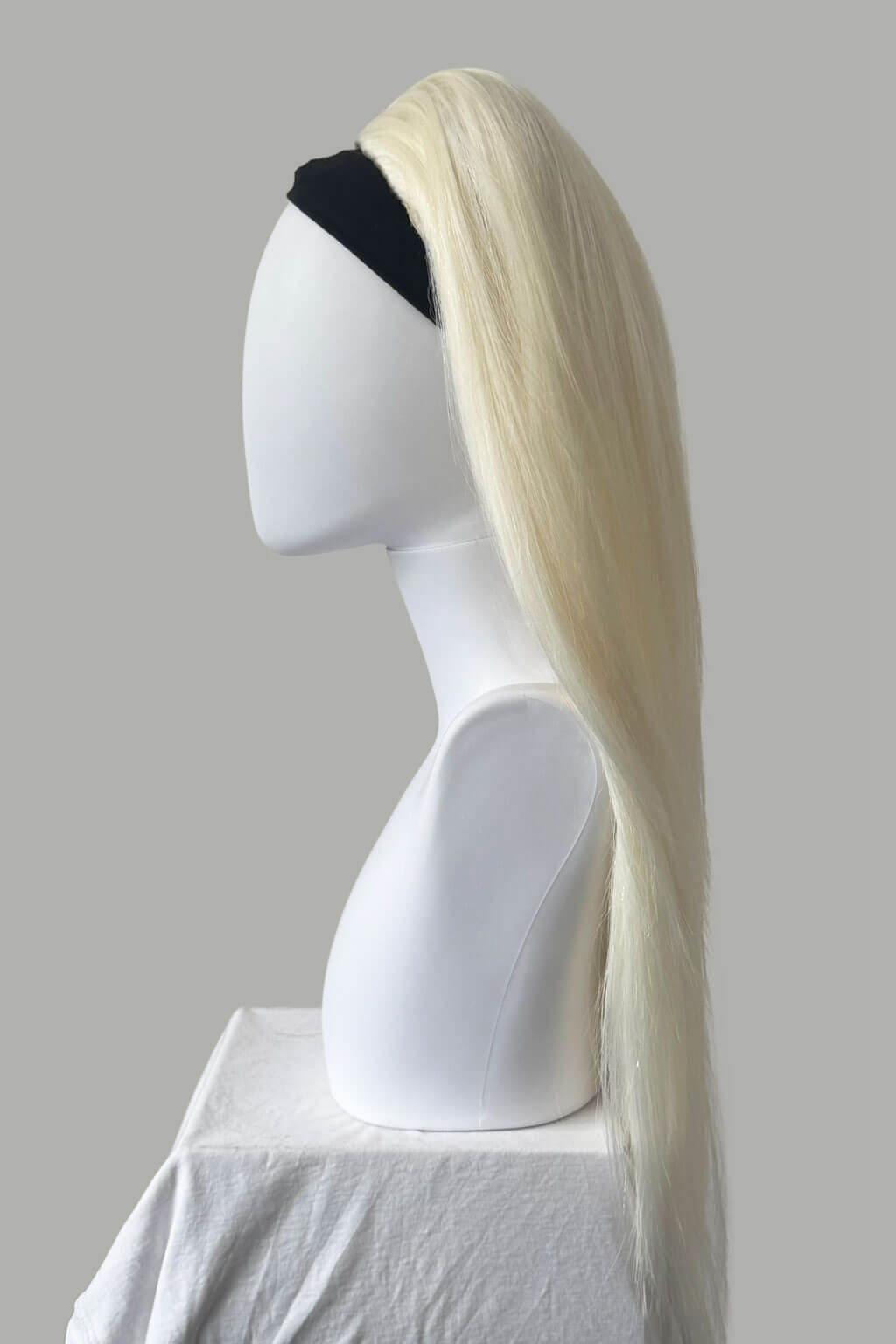 Blonde wig on a mannequin head against a gray background. 1960s style hair, high crown long straight half wig: Andrea platinum blonde 1001