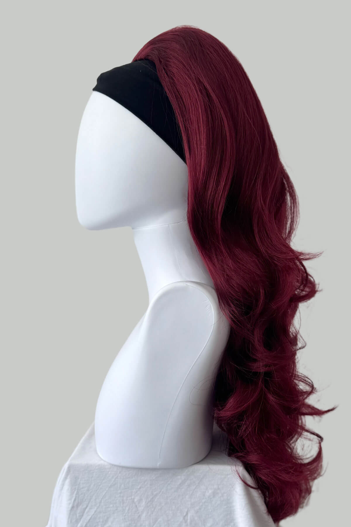 Mannequin head with burgundy wig on a plain background. High crown long, wavy half wig and volume ring, cherry red: Bardot 39