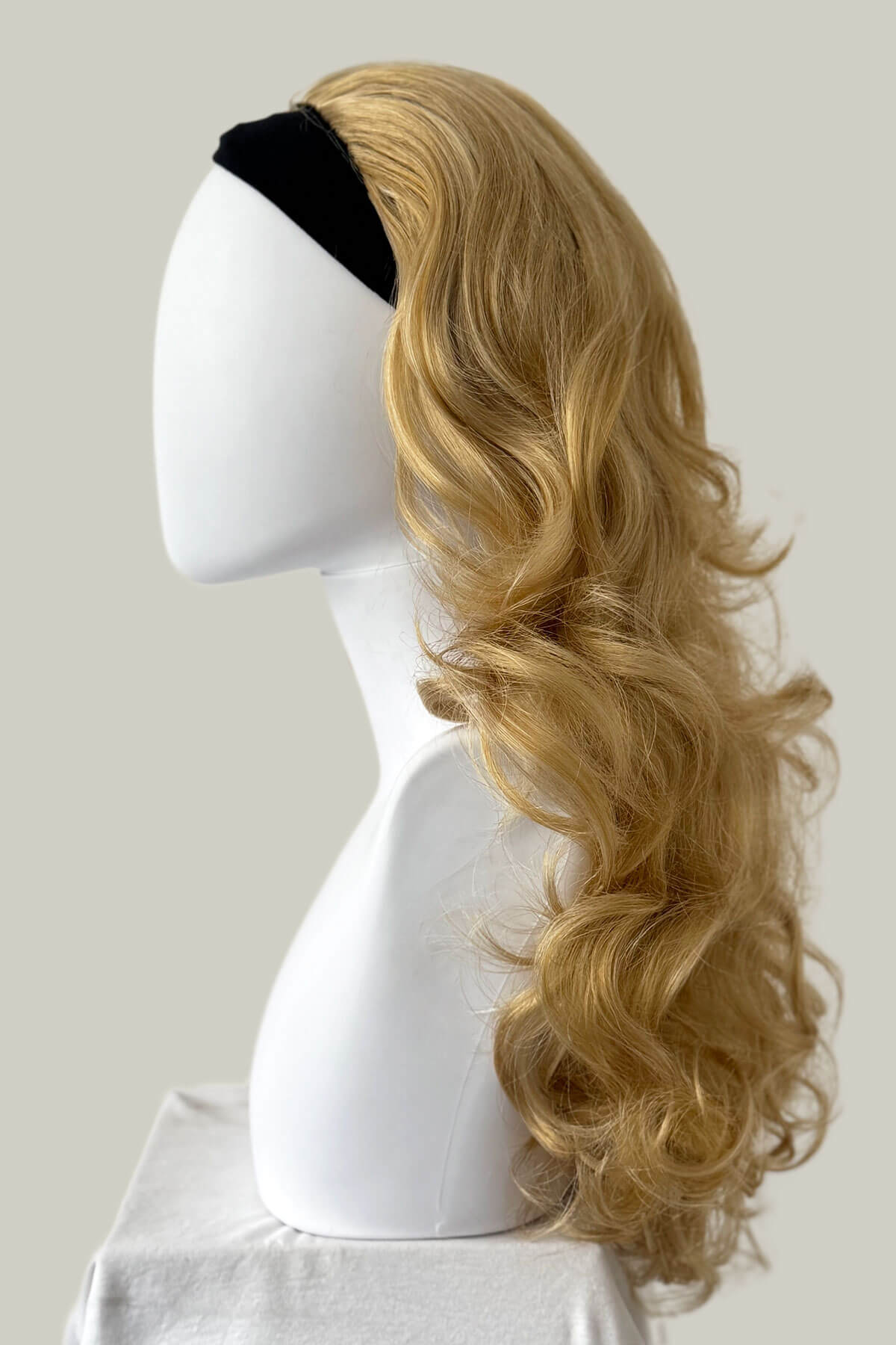 Blonde wig on a mannequin head with a black headband against a plain background. Curly blonde half wig hairpiece extension (3/4 wig), long: Meana honey blonde 24BH613