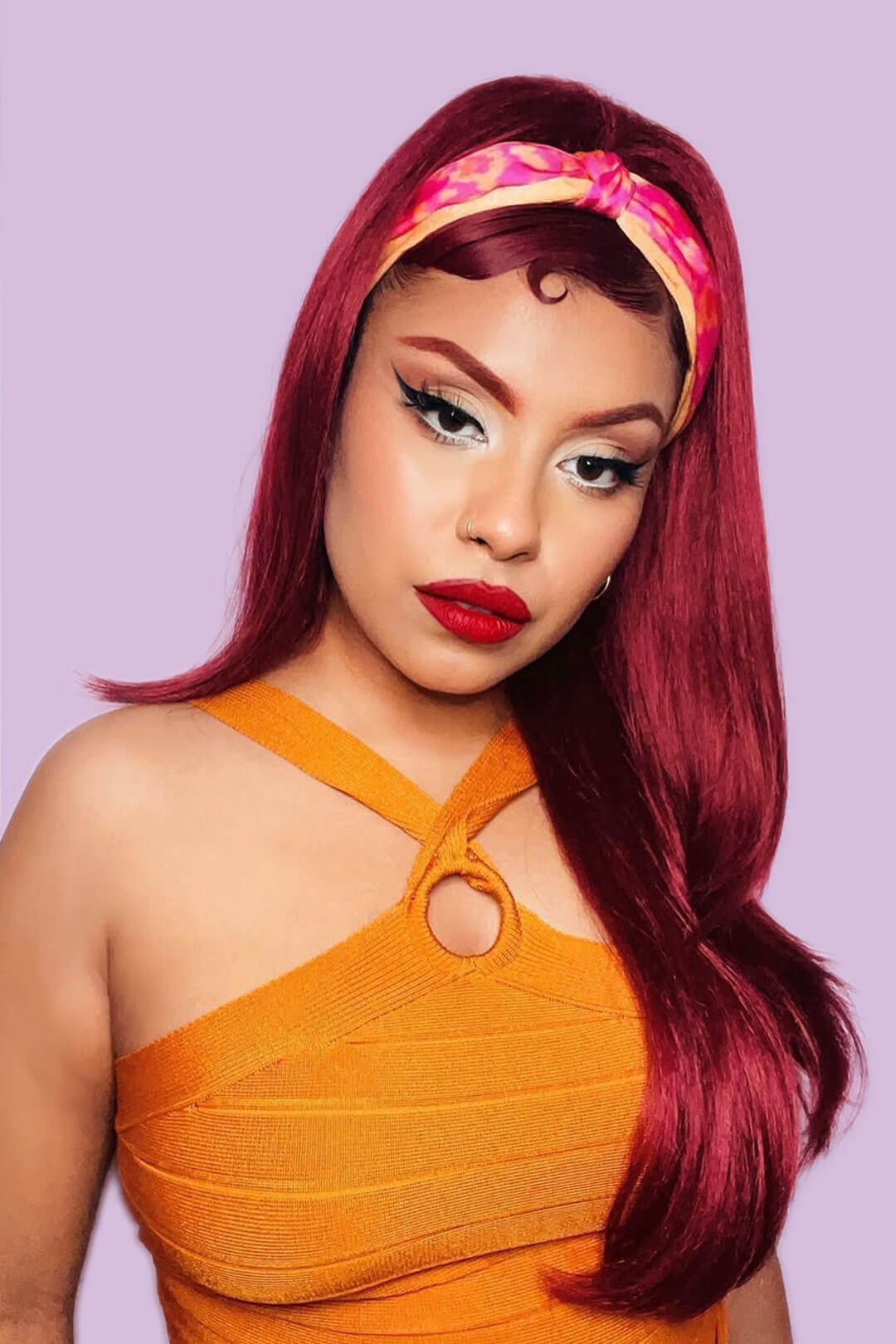 Woman with vibrant red hair and orange dress against a light purple background
