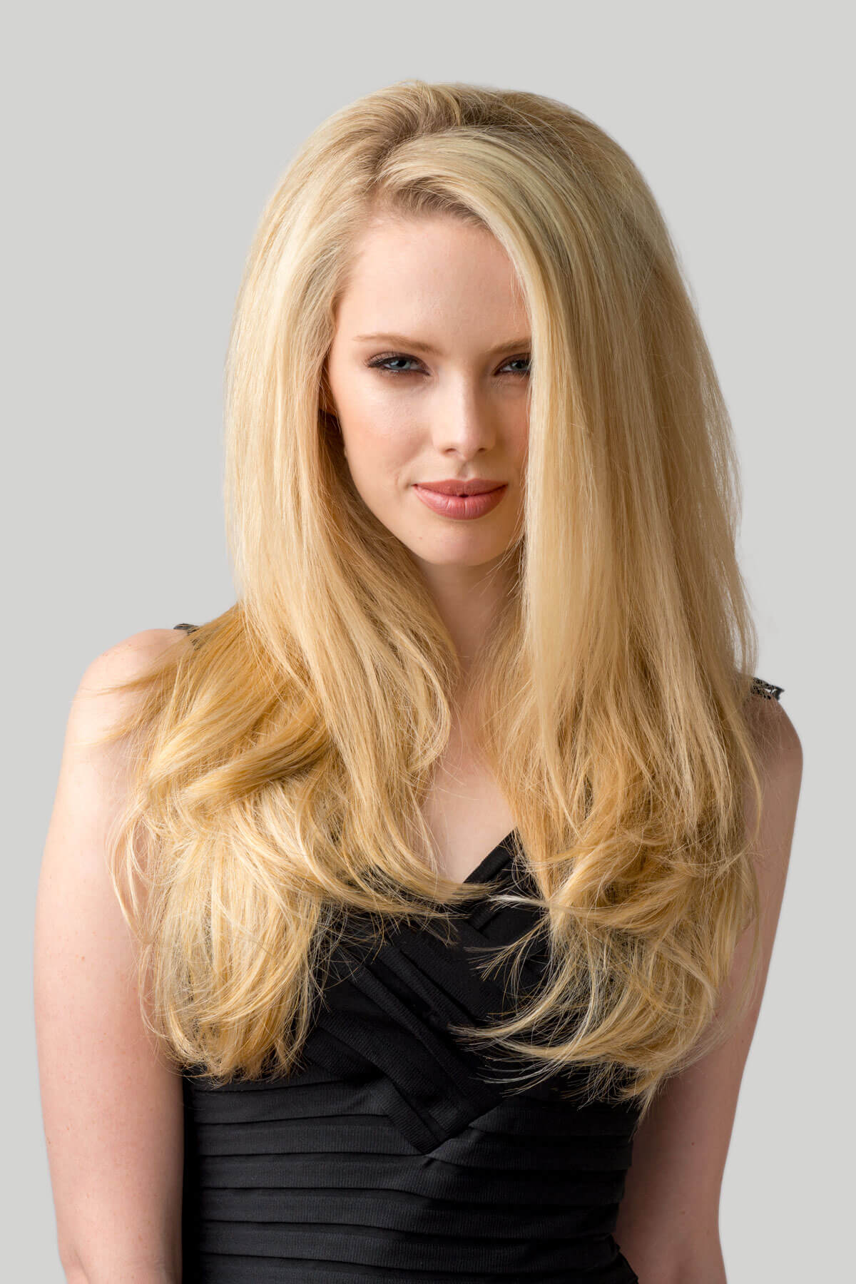 Woman with long blonde hair wearing a black dress against a gray background. Straight blonde half wig hairpiece (3/4 wig), layered: Autumn honey blonde 24BH613