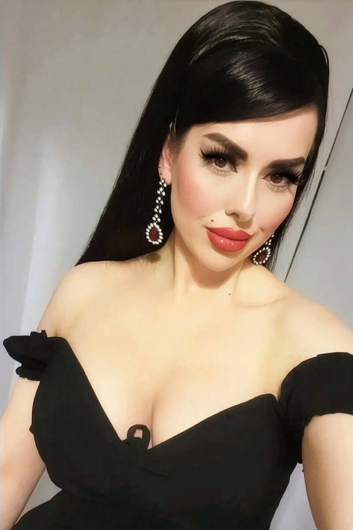 Woman wearing a black off-shoulder top with a plain background. 1960s style hair, high crown long straight half wig: Andrea black 1B