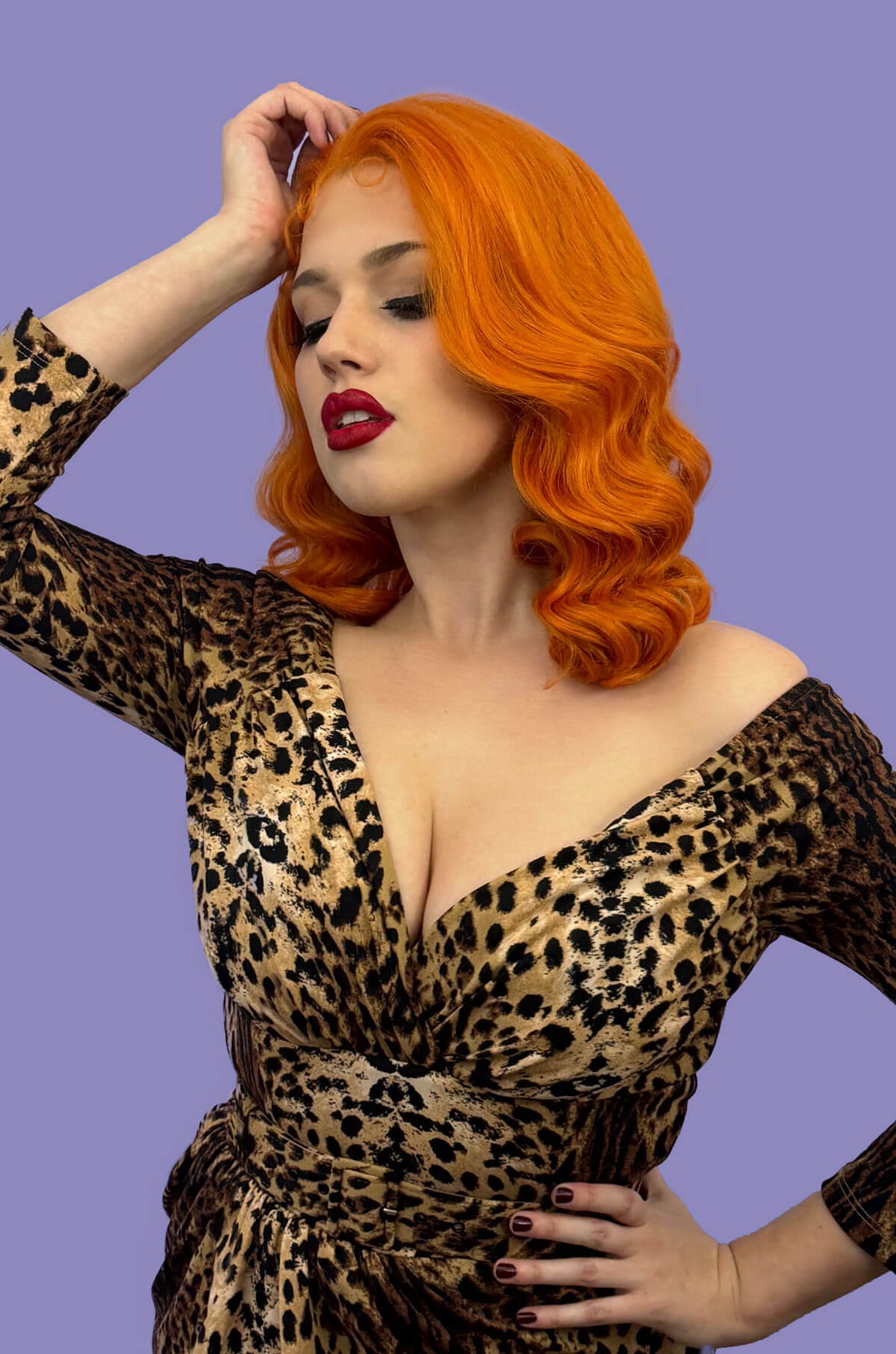Woman with vibrant orange hair and red lipstick wearing a leopard print dress against a purple background. Ginger pinup lace front wig, Dita Von Teese style vintage style wig with finger waves Lula