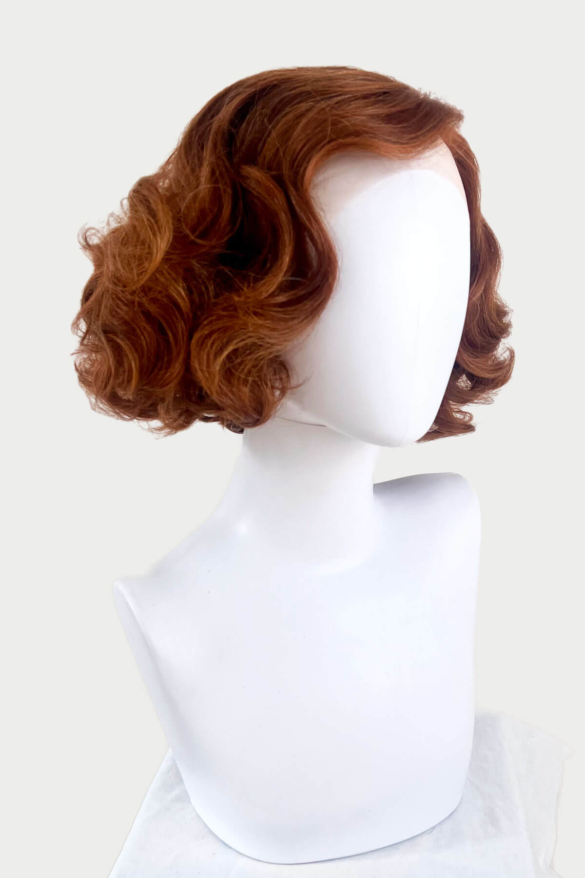 Brown wig on a white mannequin head against a white background. Auburn pinup wig, lace front, vintage style: Clementine