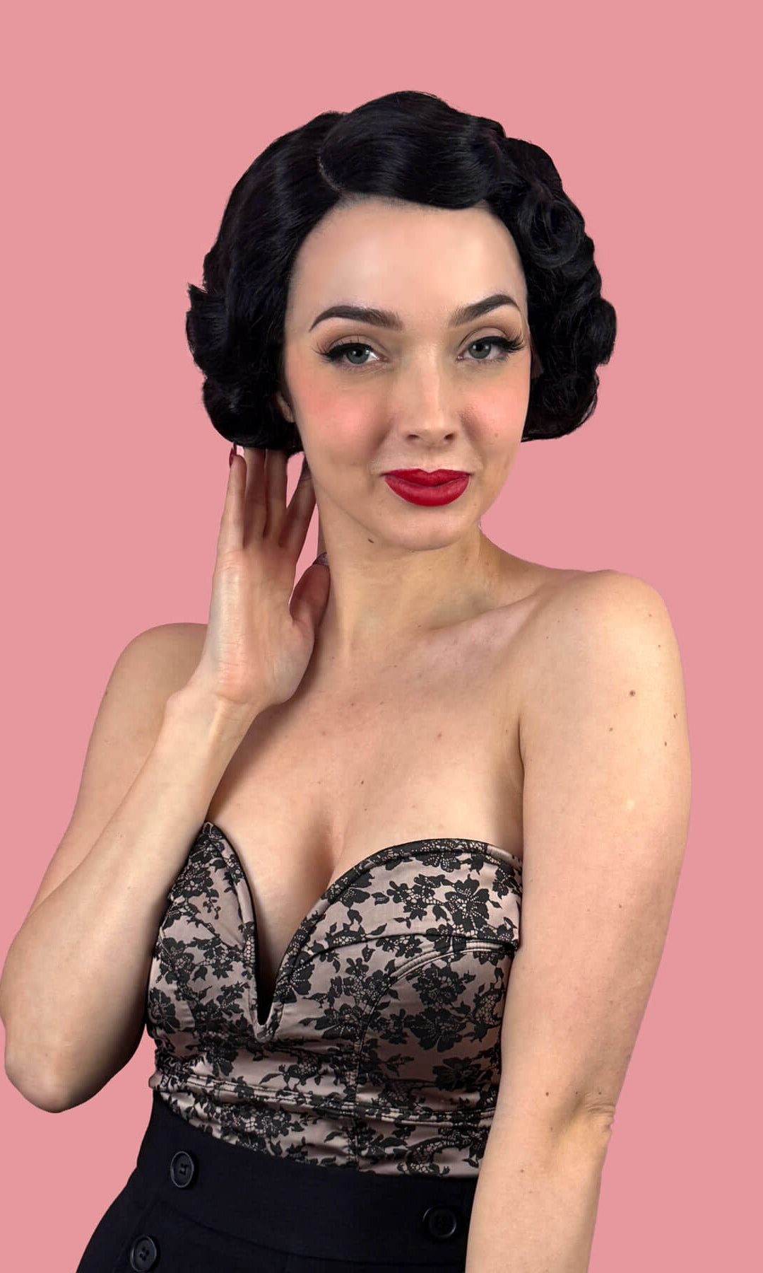 Woman with short black wavy hair against a pink background. Black lace front wig, short with finger waves: Viola