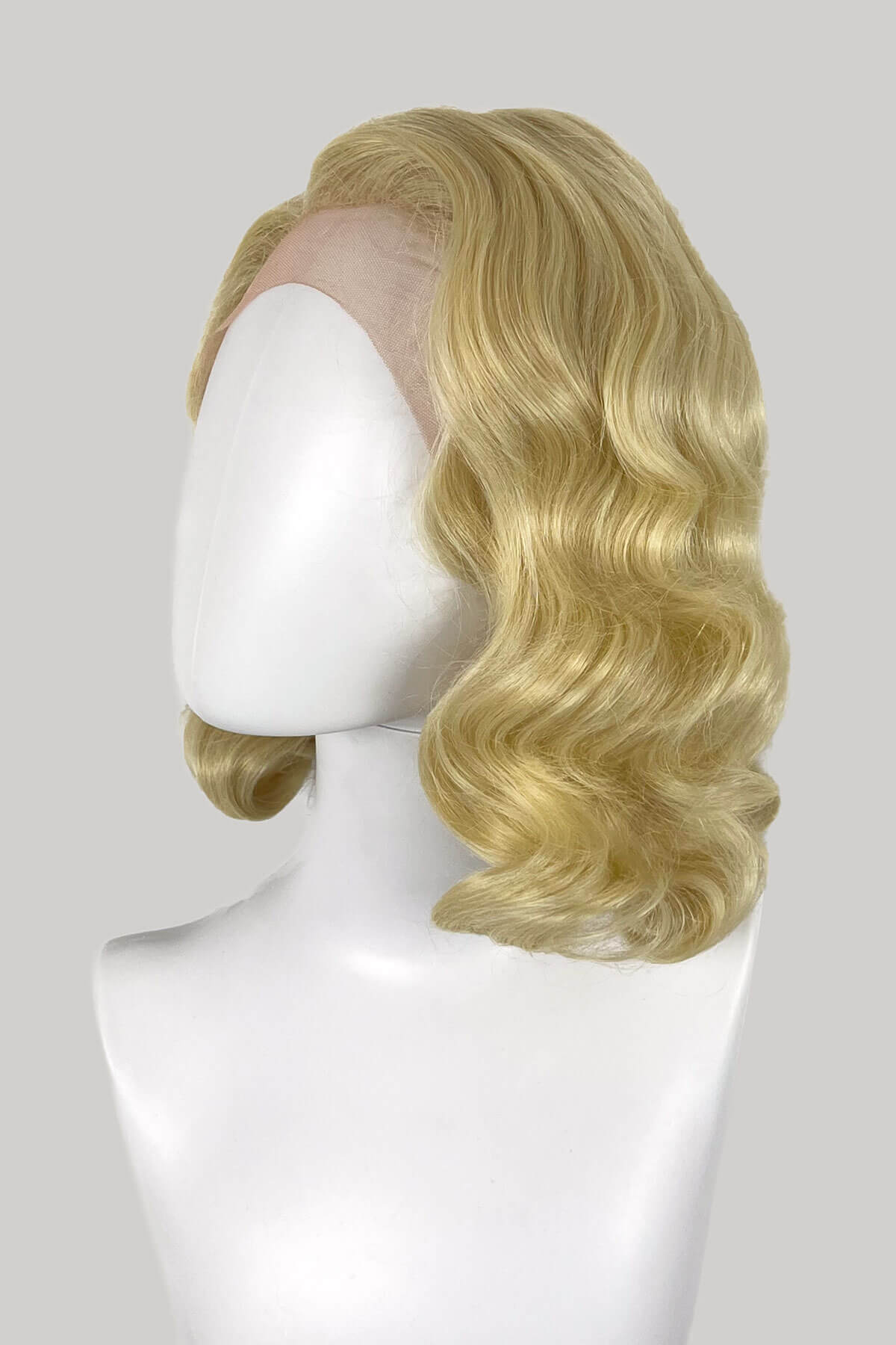 Blonde wig on a mannequin head against a white background. Blonde lacefront wig, pinup/vintage style, mid length with finger waves: Lucinda