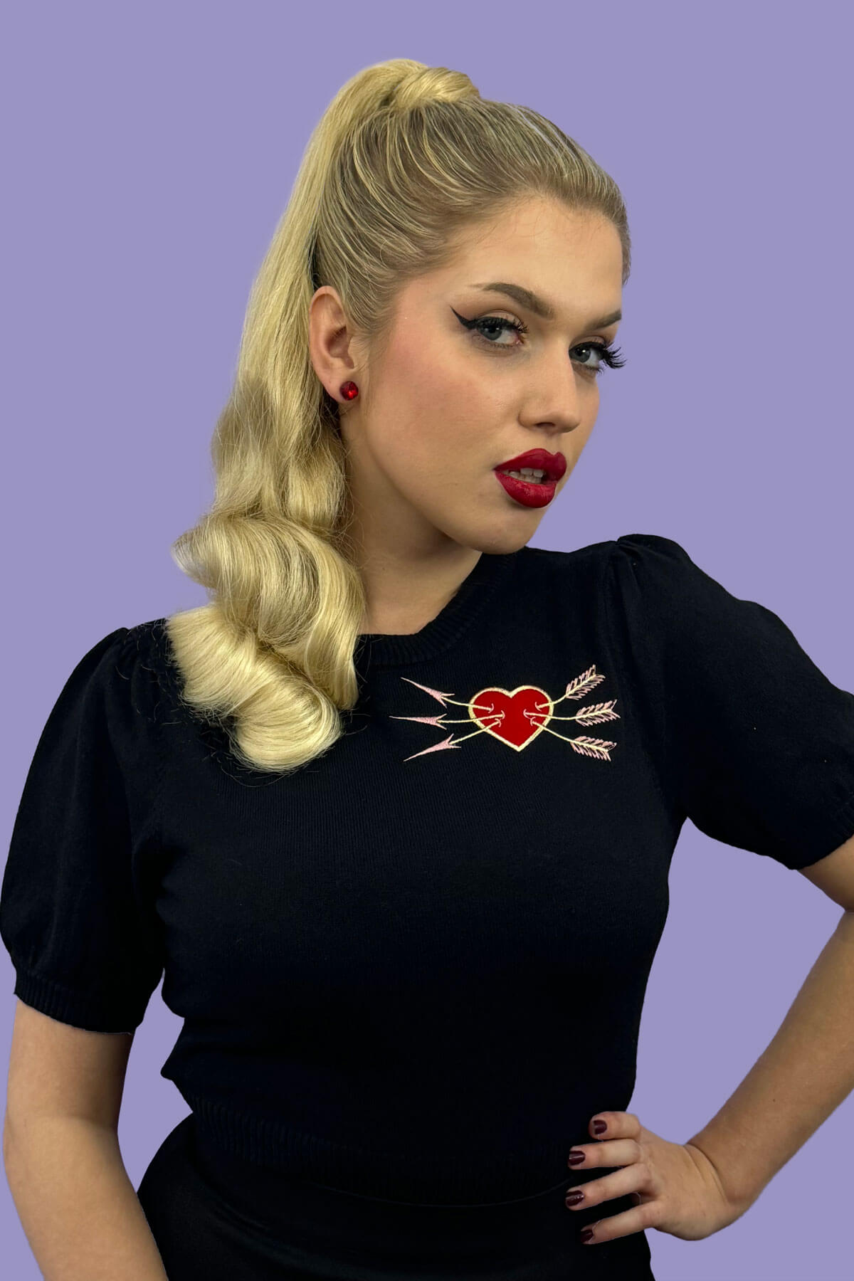 Woman wearing a black t-shirt with a red heart design on a purple background. Retro style ponytail hairpiece, long with vintage waves: Arabella