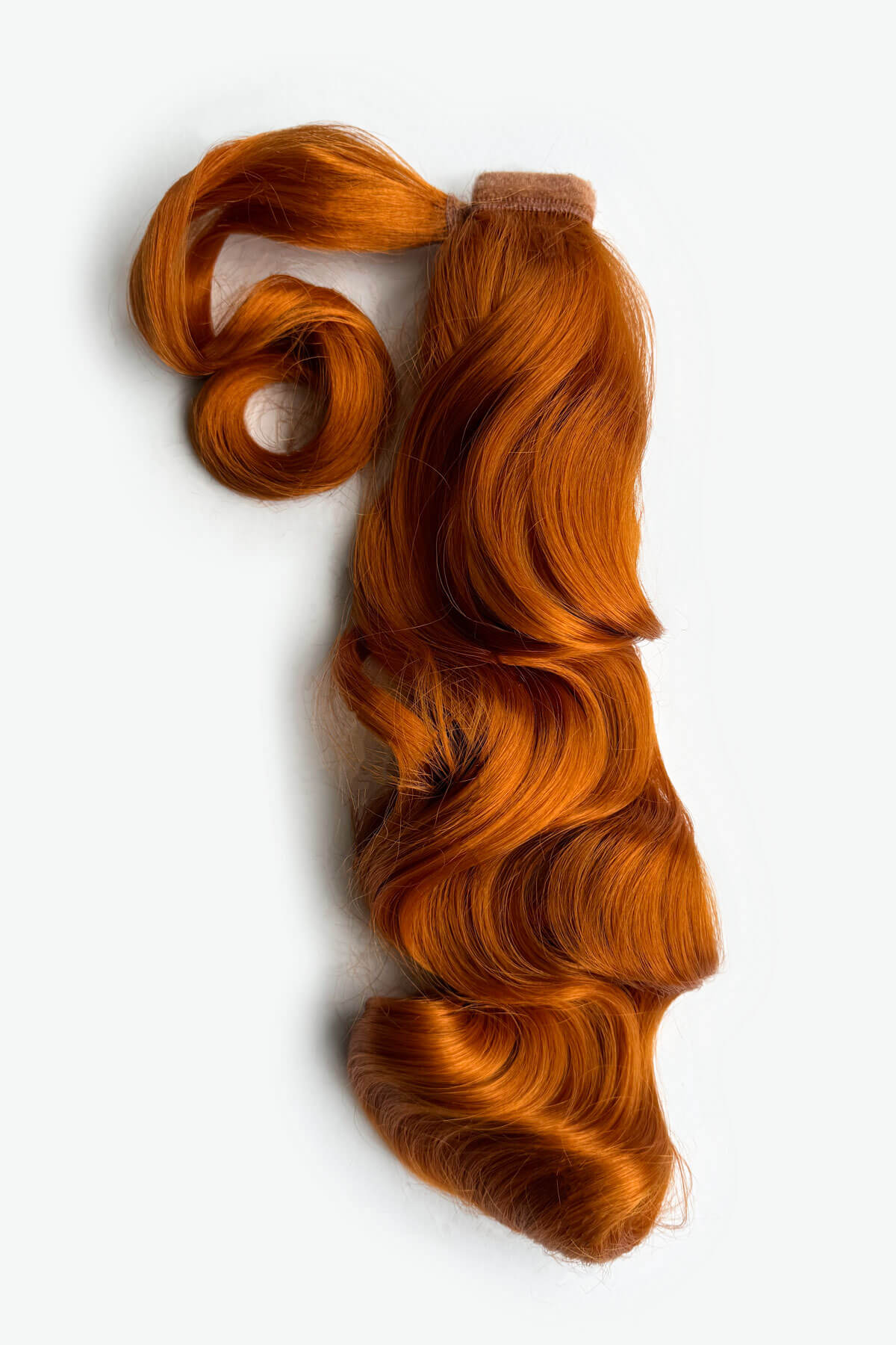 Braided hair extensions with a brown band on a white background. Retro style ponytail hairpiece, long with vintage waves: Arabella ginger