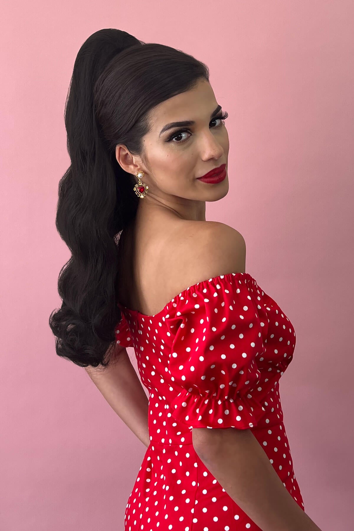 Woman wearing a red polka dot dress against a pink background. Retro style ponytail hairpiece, long with vintage waves: Arabella dark chocolate brown 6