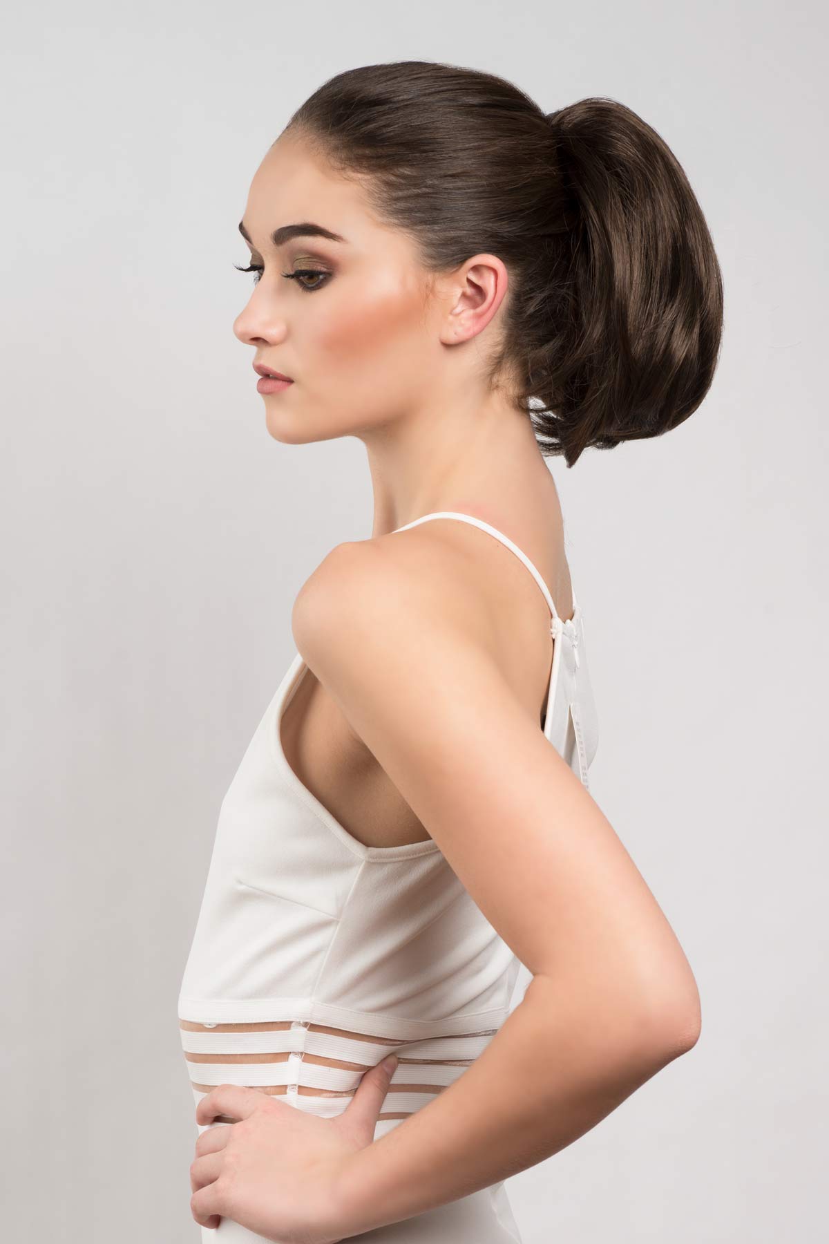 Woman wearing a white tank top against a plain background. Short ponytail extension hairpiece, straight, full & bouncy: Tanaya chestnut brown 8