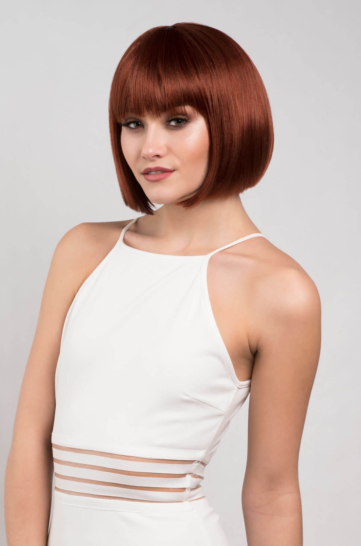 Woman with a stylish bob haircut wearing a white dress against a plain background.Short copper-red/ginger bob wig: Minnie